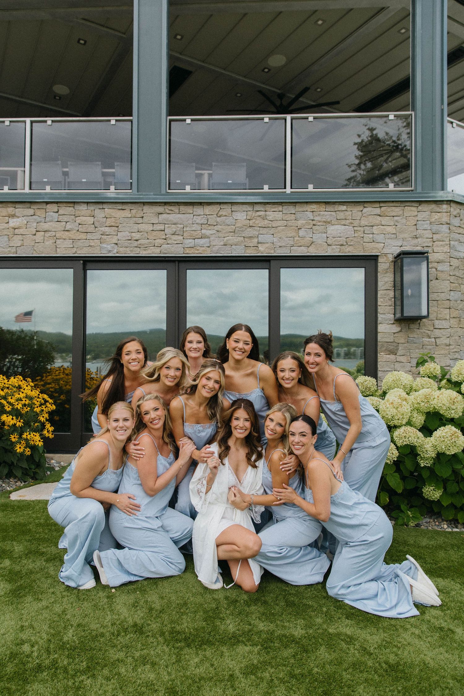 Bride in white gown poses with bridesmaids in light blue dresses outdoors at elegant venue.