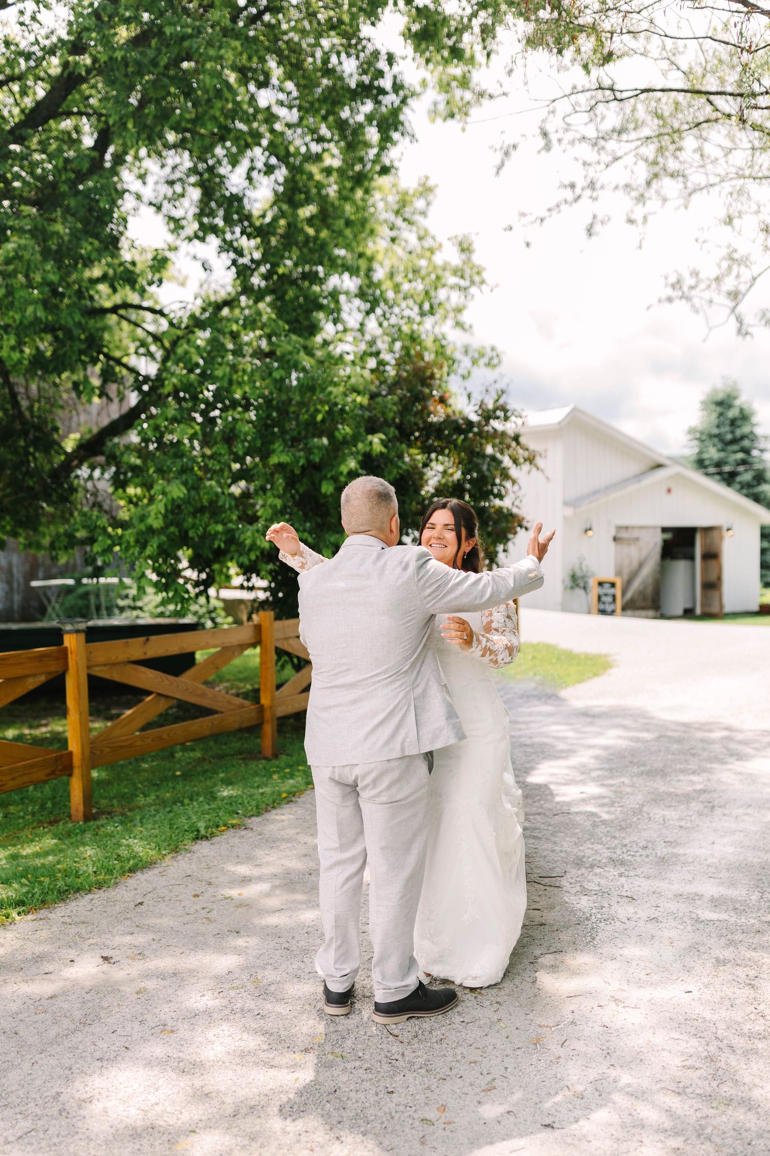 Joyful bride and groom embrace and dance on a gravel path during their outdoor wedding first look.
