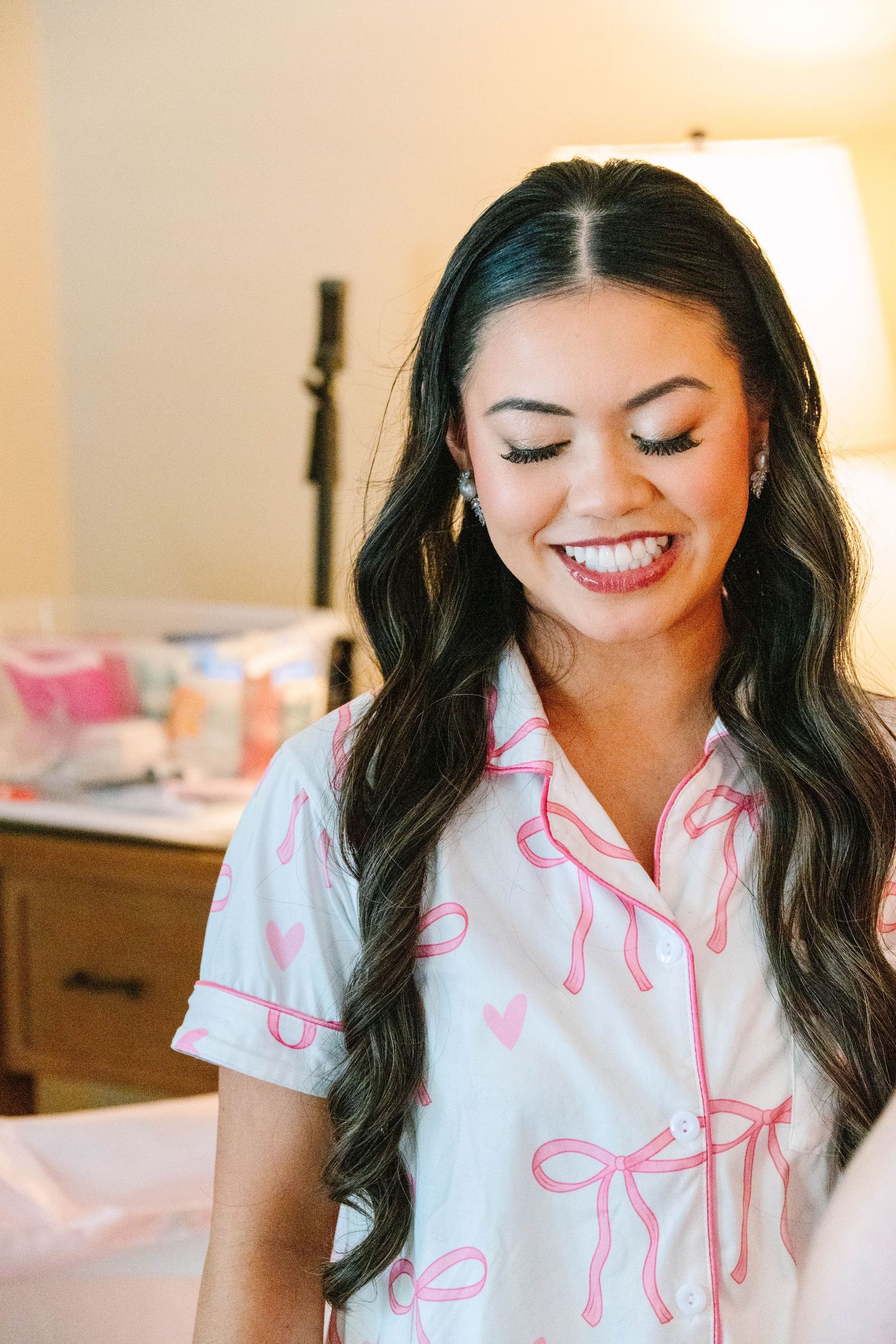 Bride laughing in white and pink bow-print pajamas in hotel room.