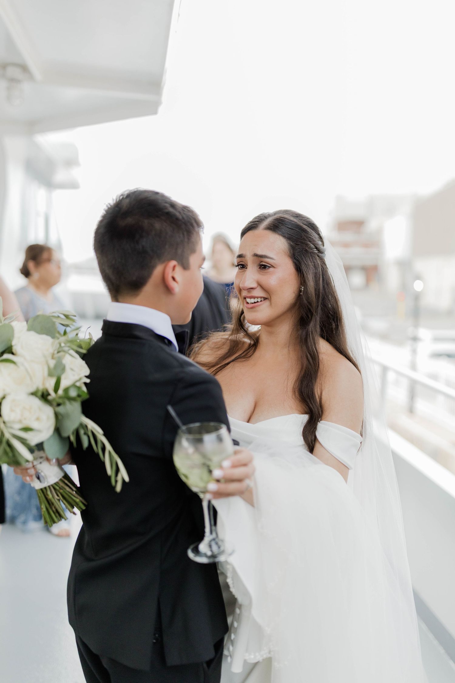 Bride holding wine glass and white bouquet shares emotional moment with groom on yacht wedding venue.