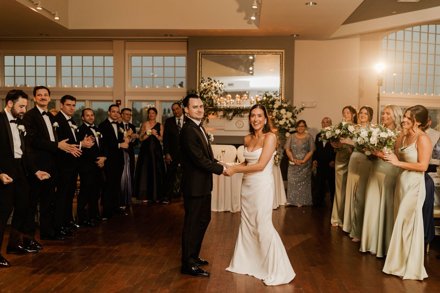 Couple sharing first dance at elegant wedding reception surrounded by guests and bridesmaids.