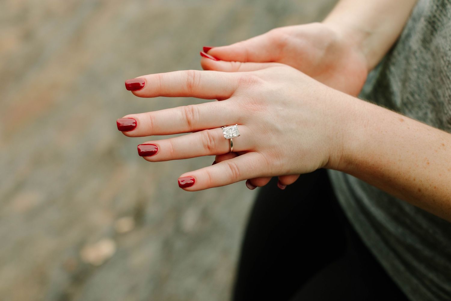Close-up of a woman's hand with red nails wearing a diamond engagement ring on her ring finger.