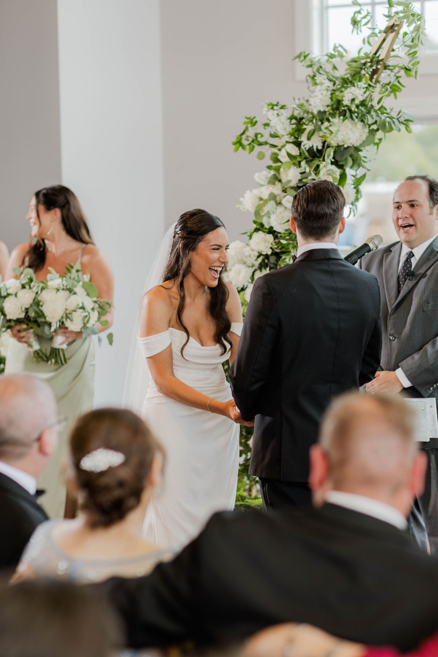 Bride laughing joyfully with groom at altar during wedding ceremony with floral arch.