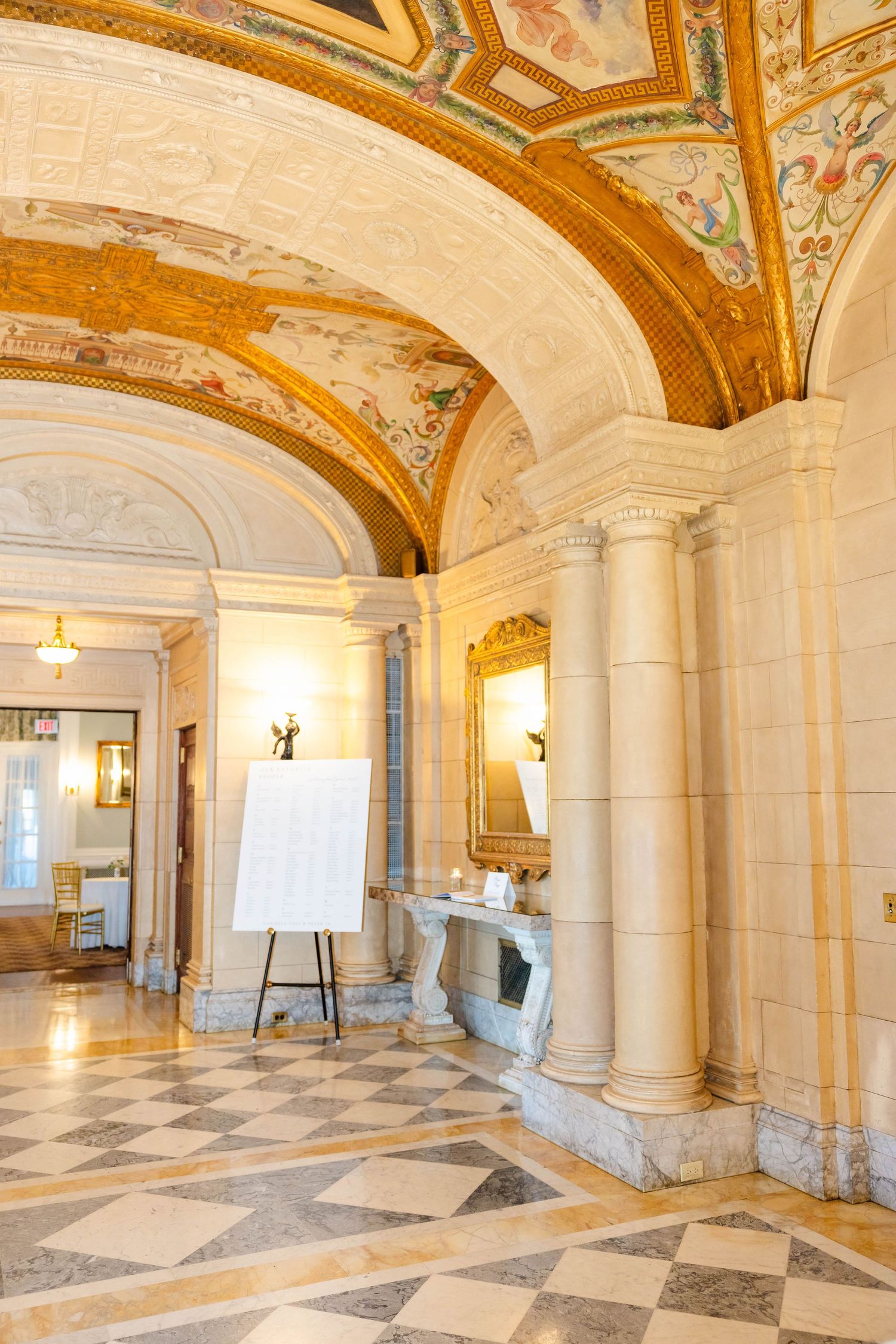Elegant wedding venue interior with ornate gilded vaulted ceiling, marble floors, and fireplace.