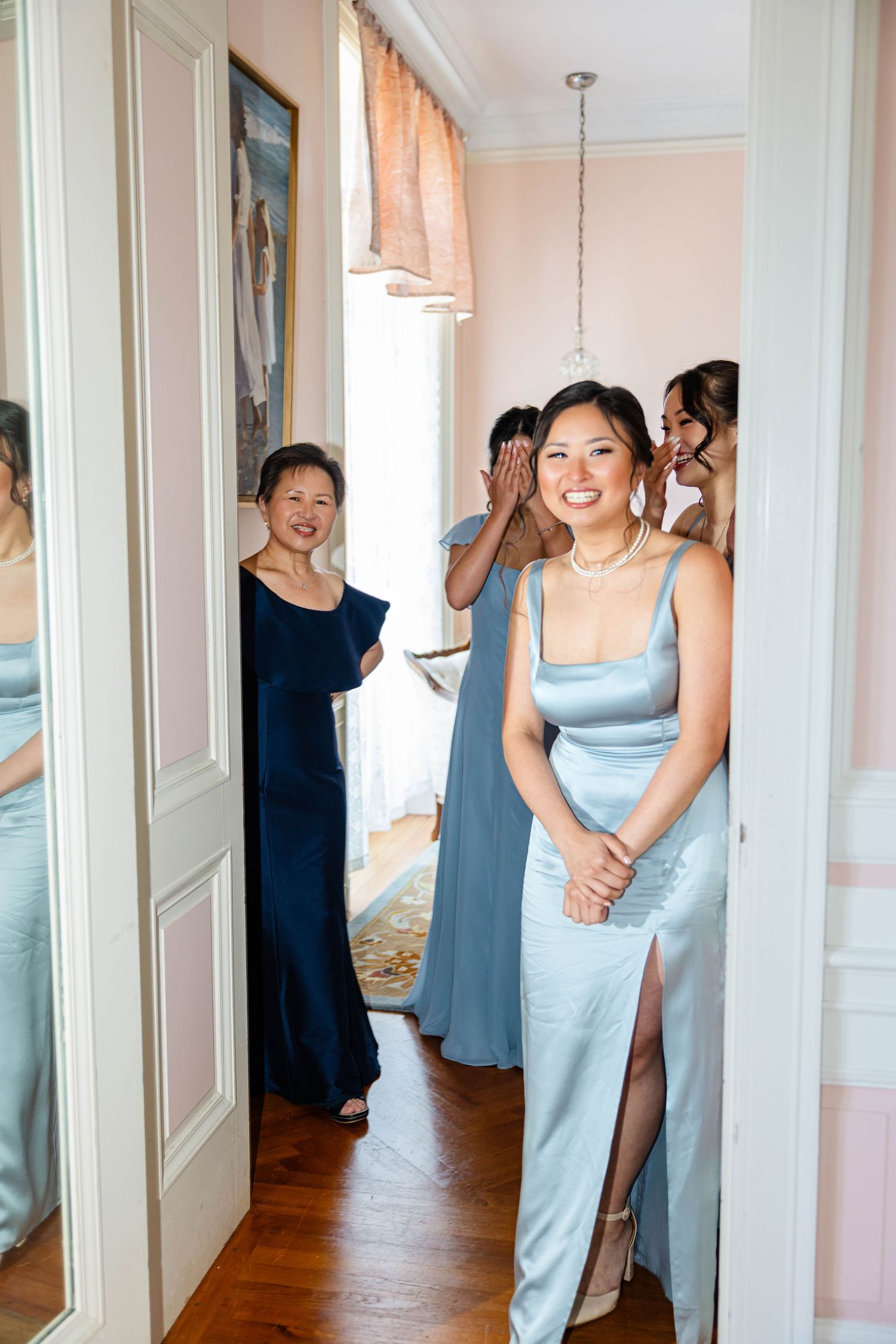 Bridesmaids in blue satin gowns smiling and reacting in a bright elegant dressing room.