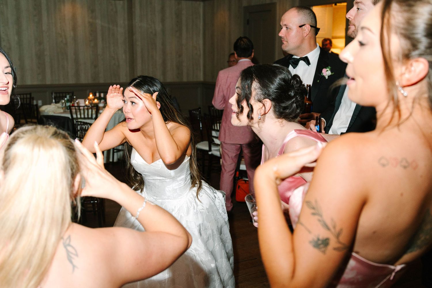 Bride laughing and dancing with bridesmaids at lively wedding reception party.