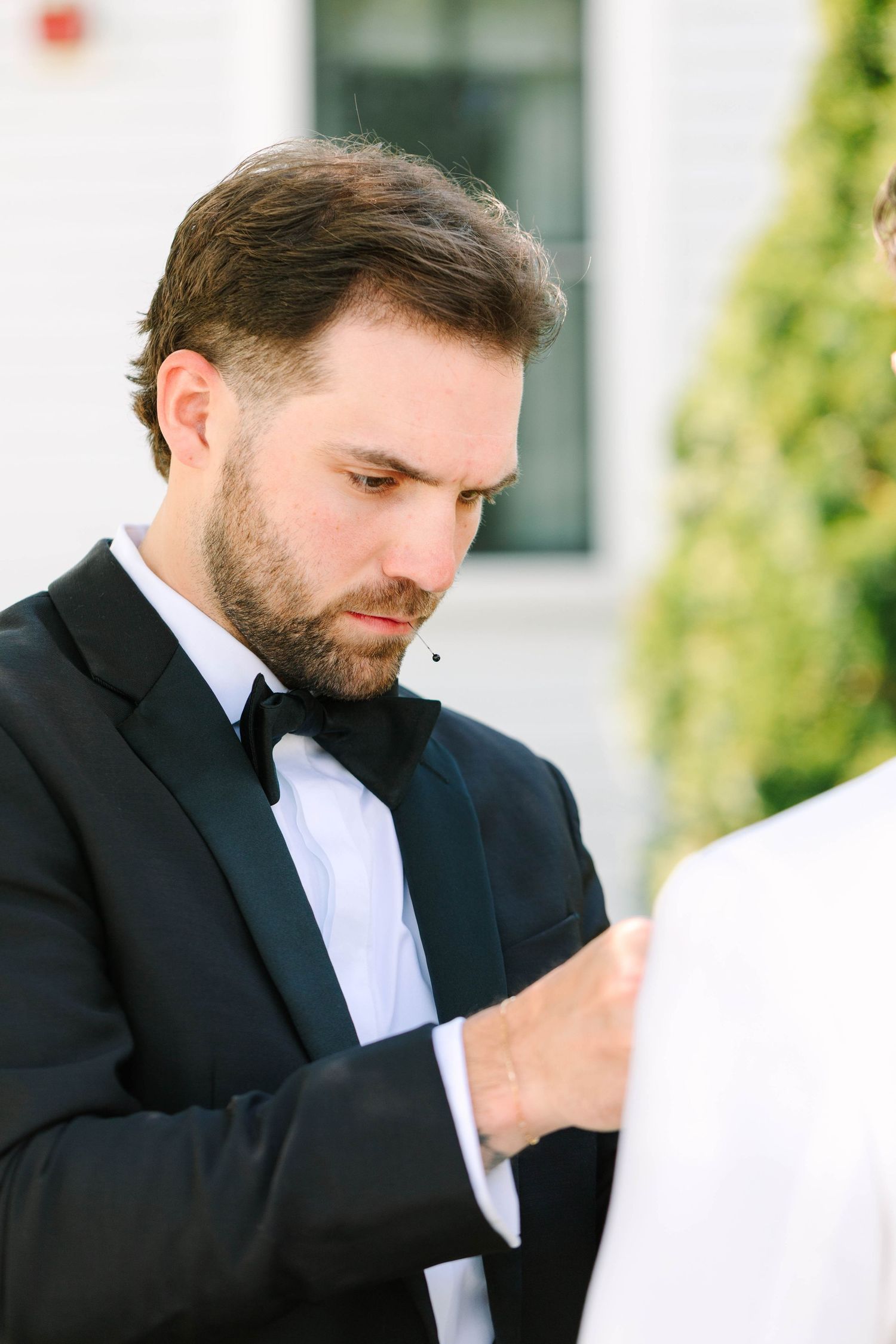 Man in black tuxedo with bow tie carefully adjusting another persons white shirt cuff outside.