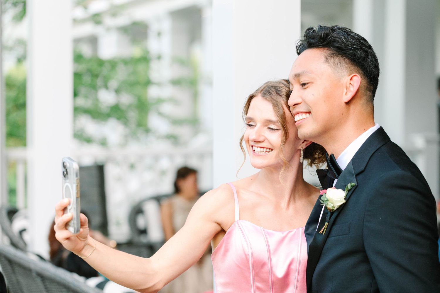 Smiling couple takes a selfie at a wedding reception, woman in pink dress and man in suit.