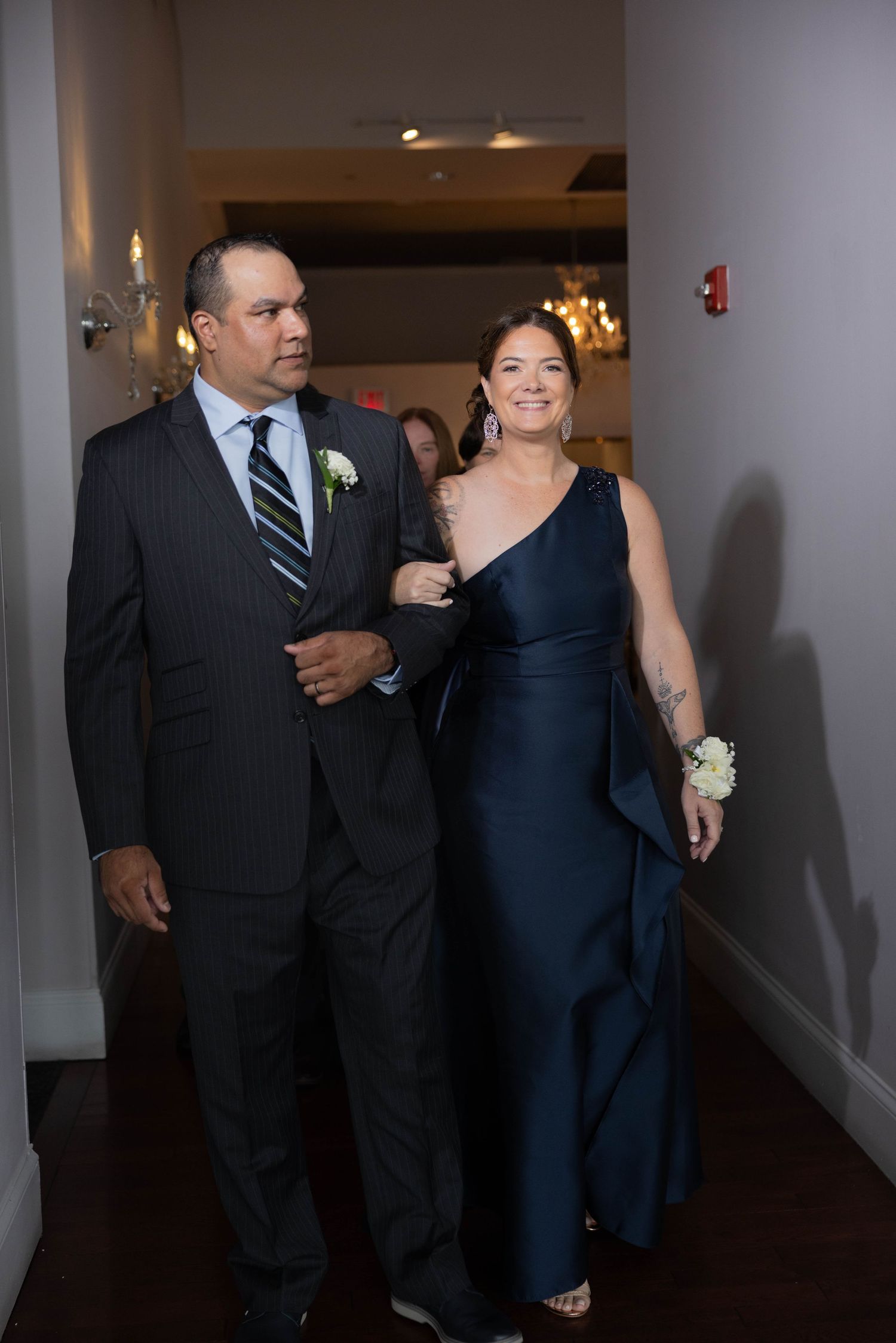 Elegant couple in formal attire walking together at a wedding event, man in dark suit, woman in navy gown.