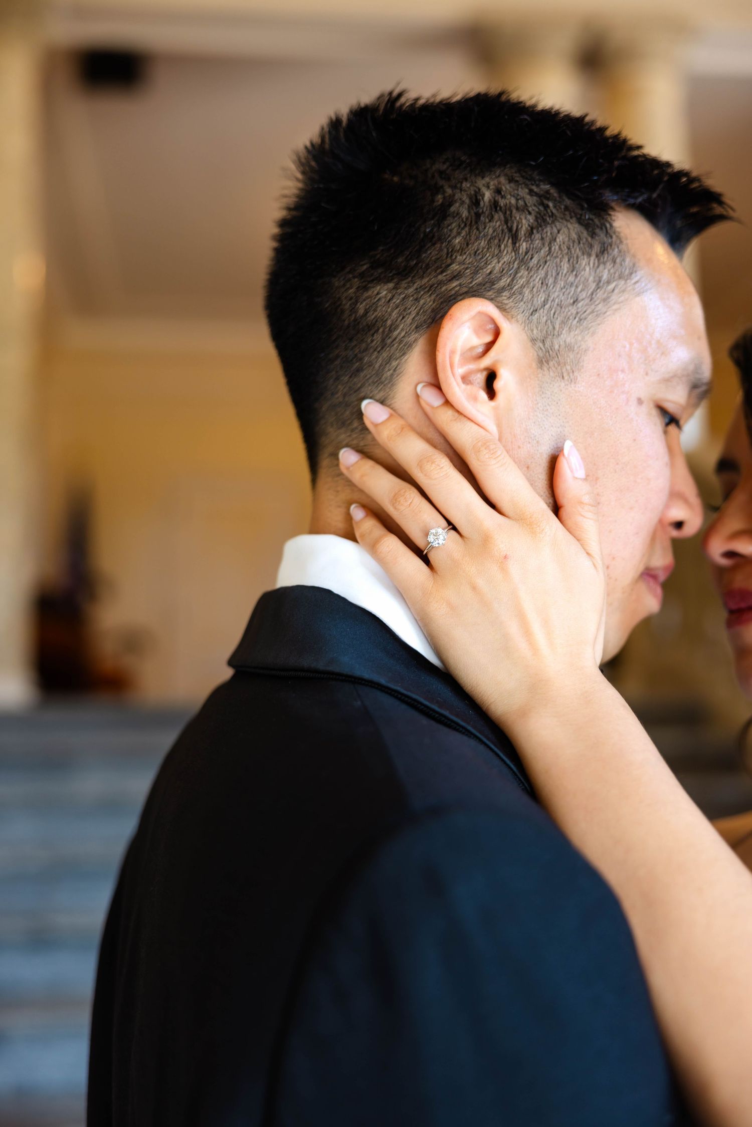 Close-up of bride's diamond engagement ring as she tenderly holds groom's face at wedding.