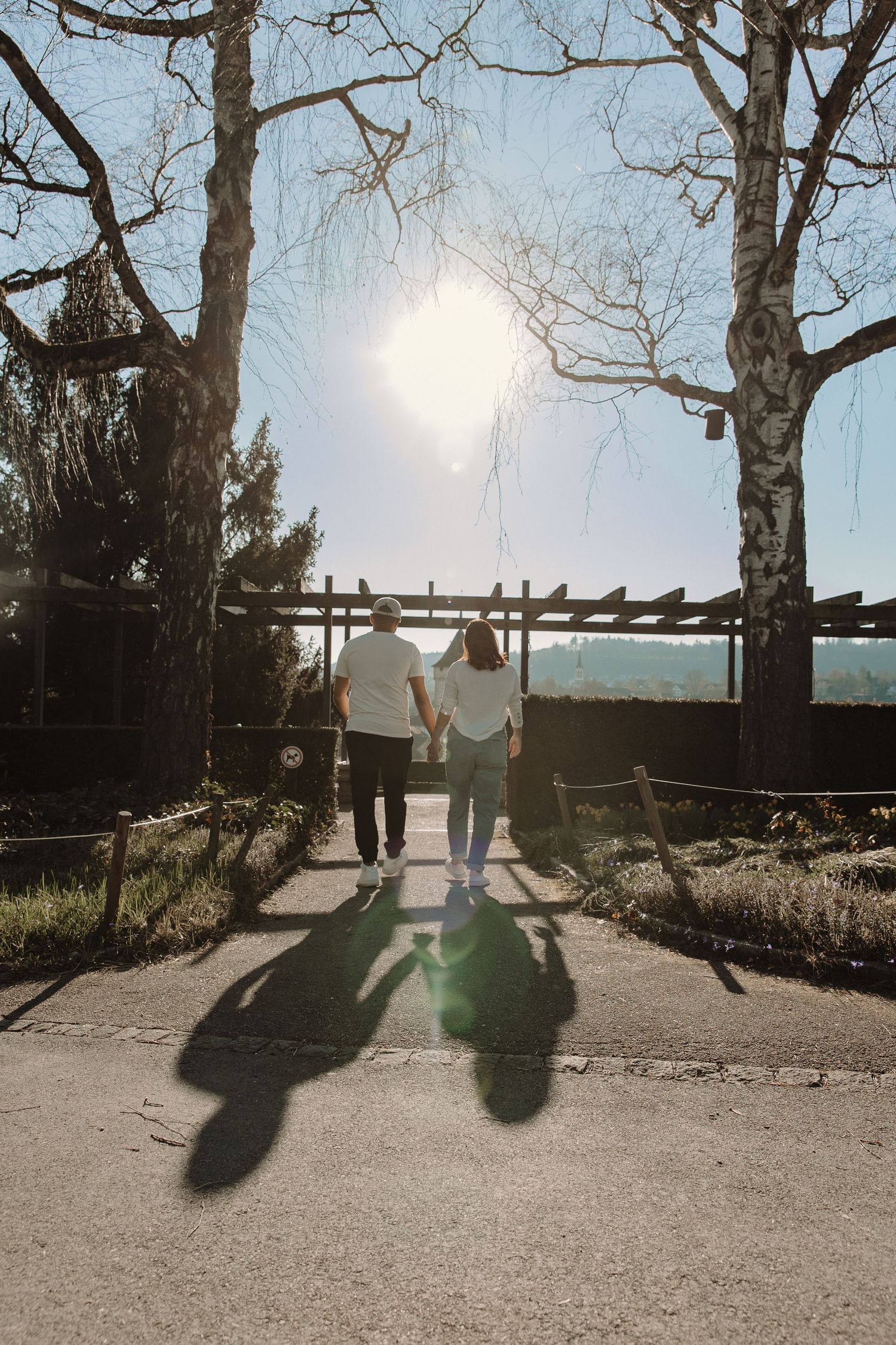 Silhouetted couple holding hands while walking toward sunset under wooden pergola.