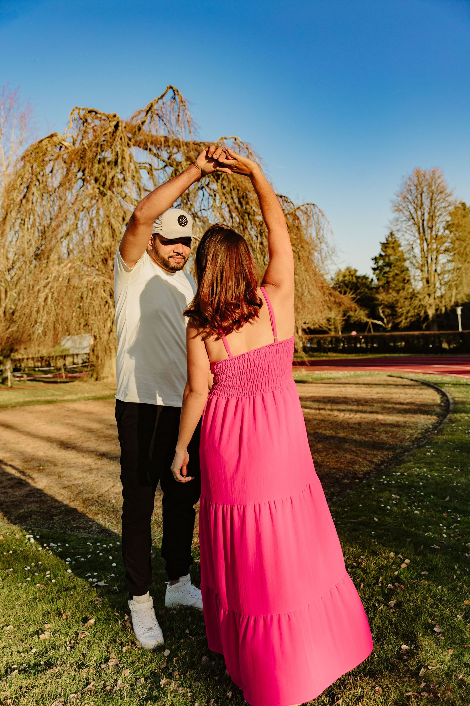 Dancing couple in pink dress and white shirt pose beneath a drooping willow tree.