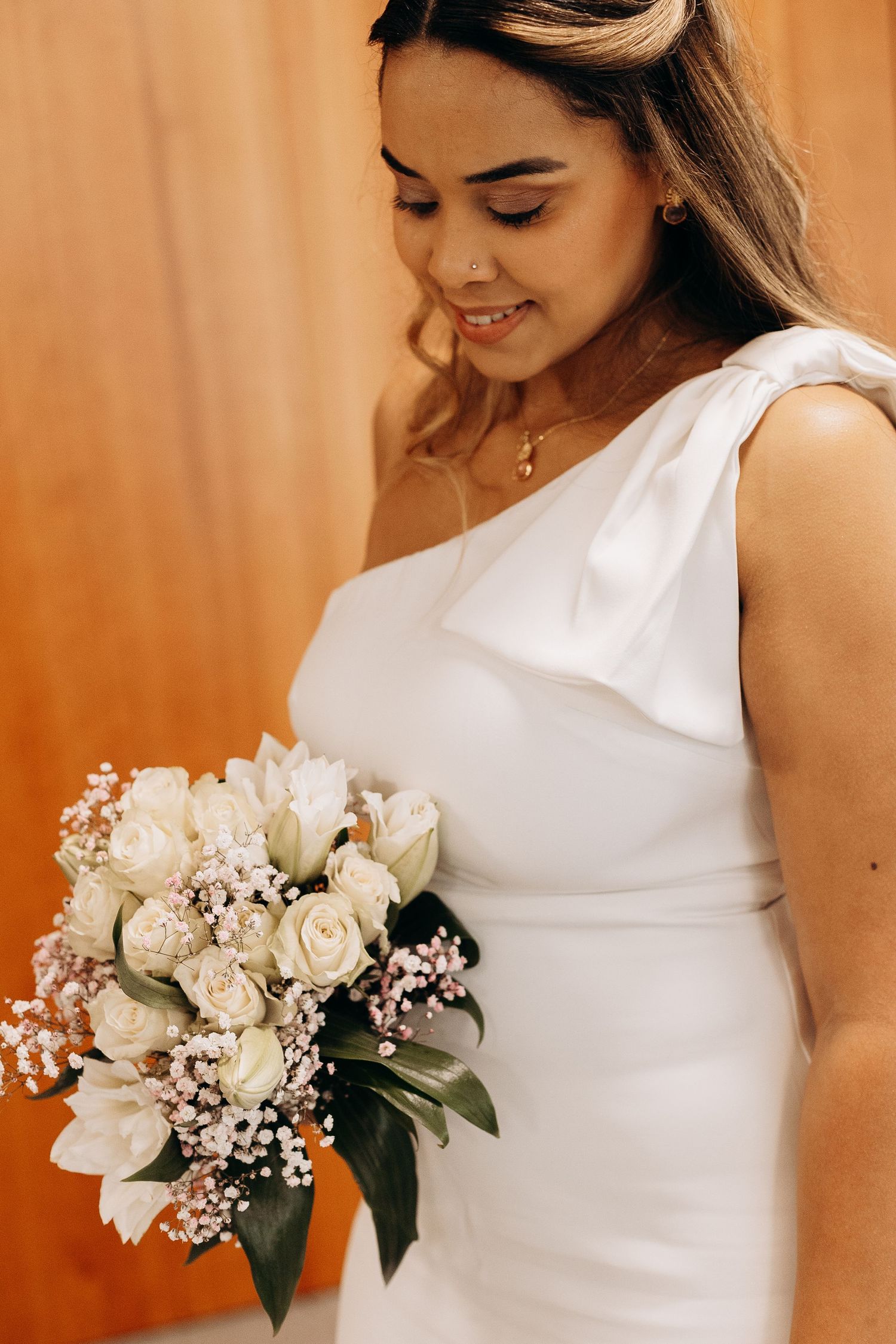 Bride in elegant white one-shoulder dress holding classic white and pink bouquet.