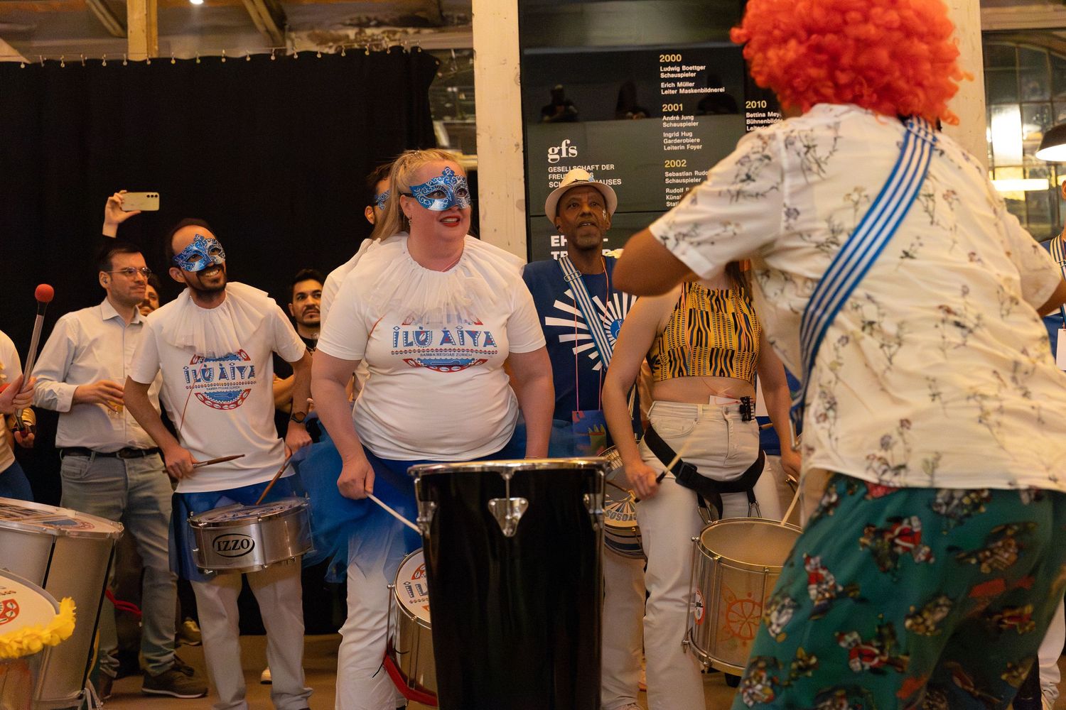 Performers in matching t-shirts and costumes gather during what appears to be a music rehearsal.