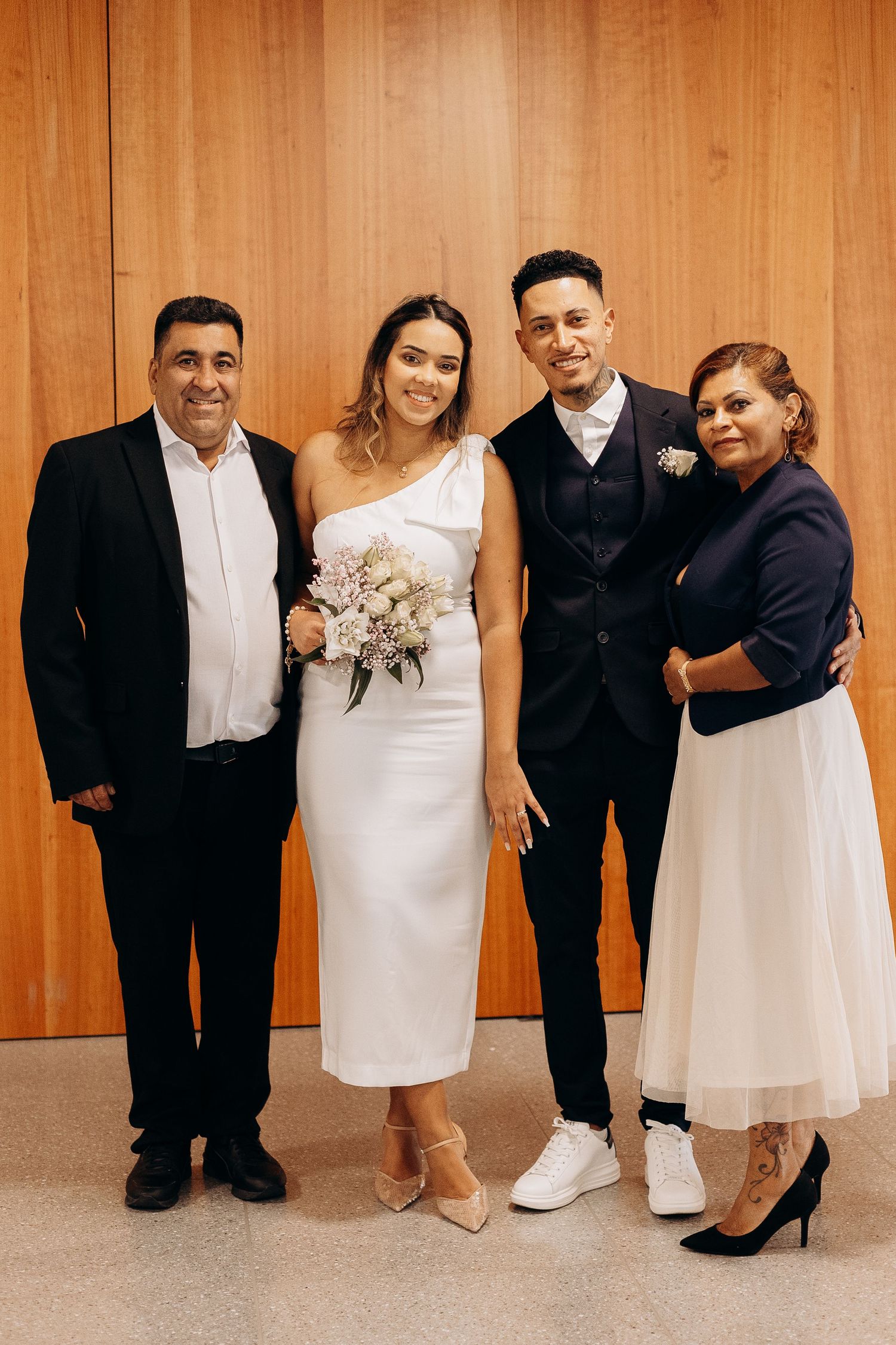 Wedding party group photo against wooden wall with formal attire and bouquet.