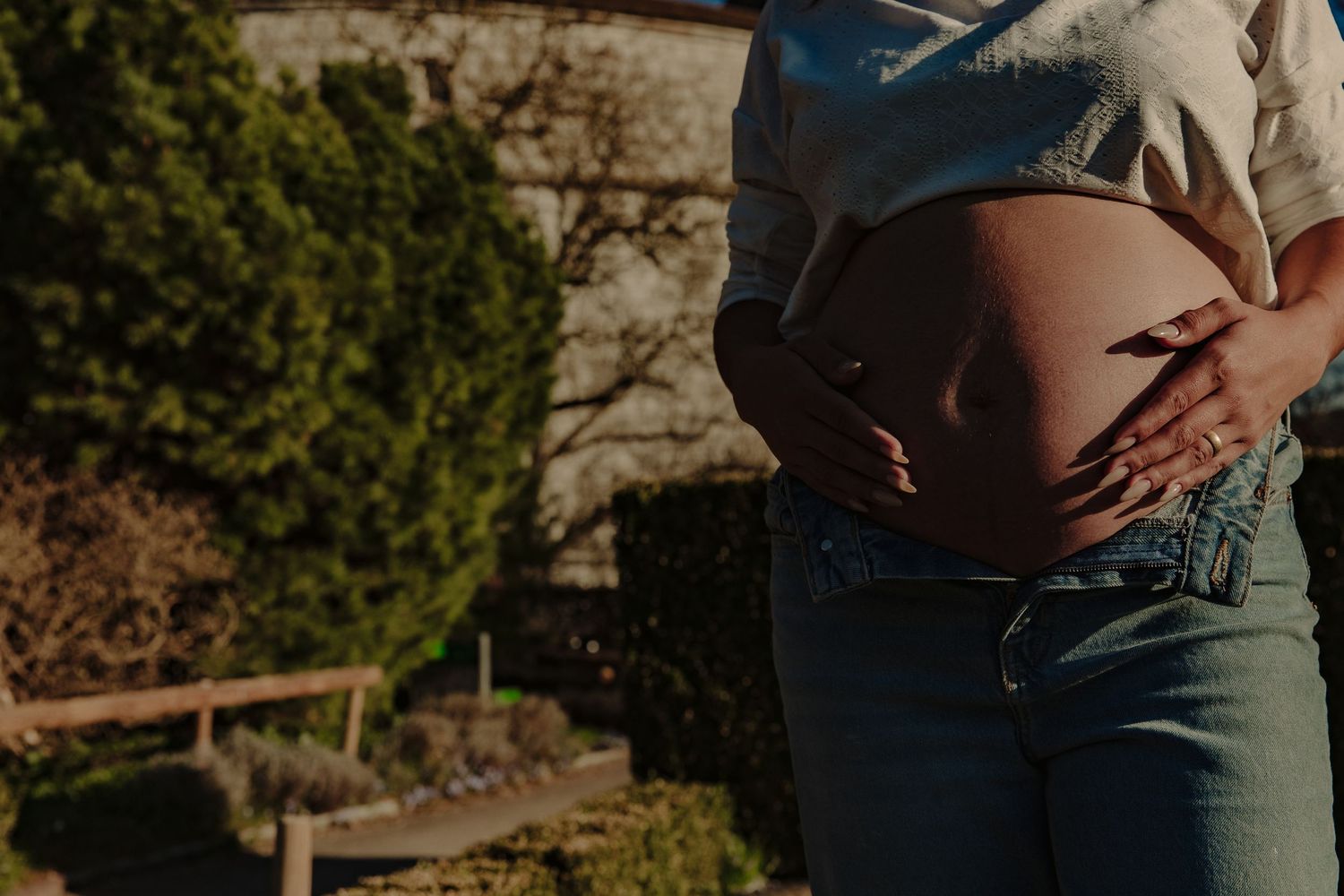 Close-up profile of pregnant belly in denim against natural outdoor backdrop.