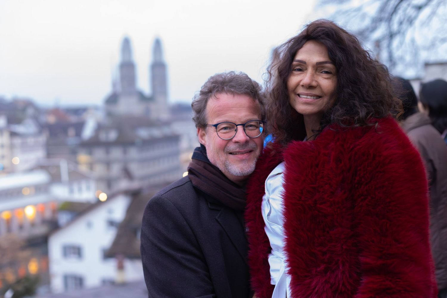 A couple poses for a winter portrait with Zurich's historic skyline behind them.