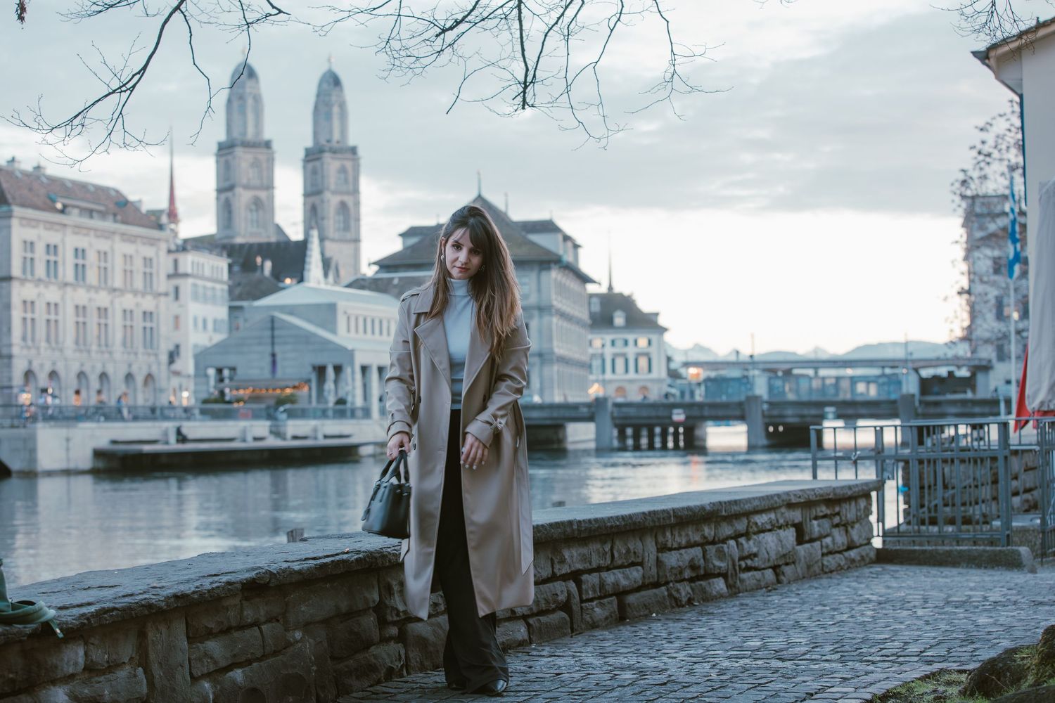 A scenic view of the Grossmünster cathedral towers along the Limmat River in Zurich on a cloudy day.