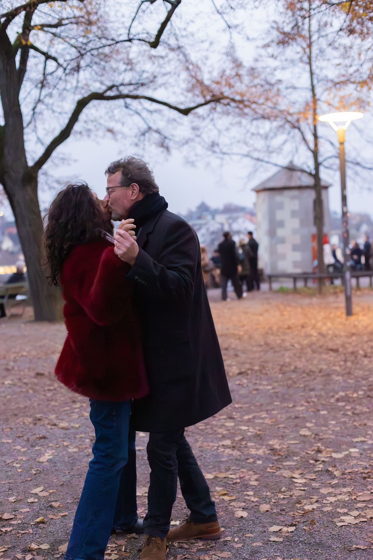 A couple shares a romantic dance among fallen leaves at dusk in a city park.