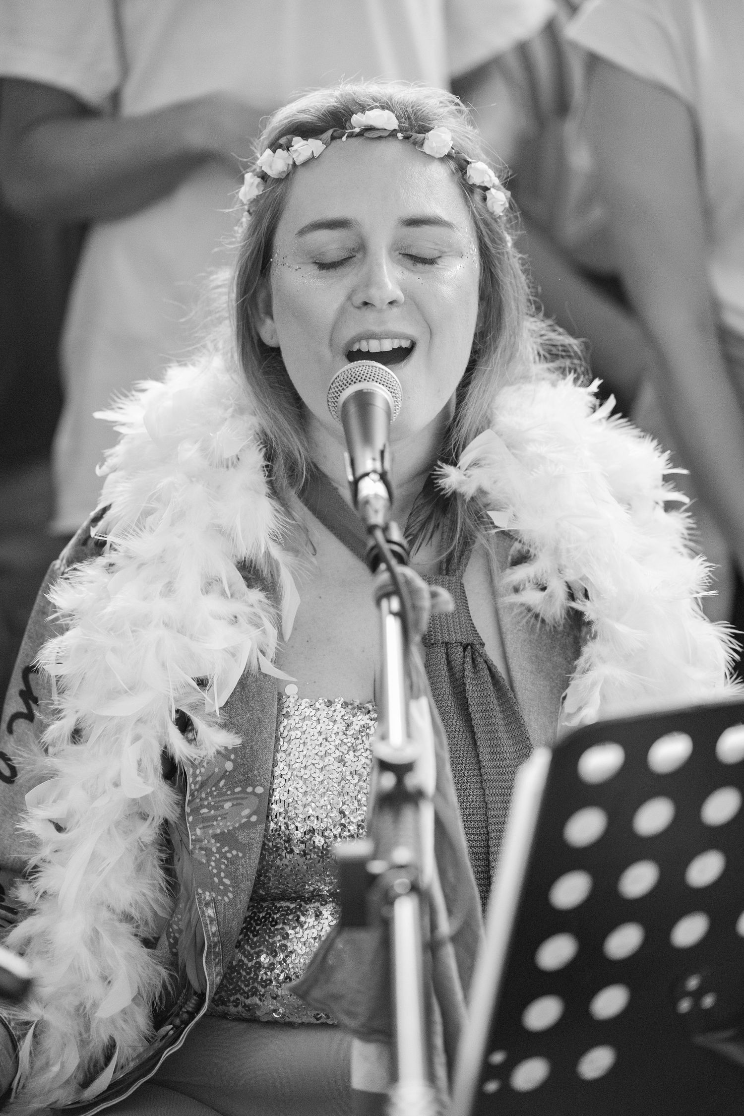 Black and white photo of singer in feather boa performing at microphone with music stand.