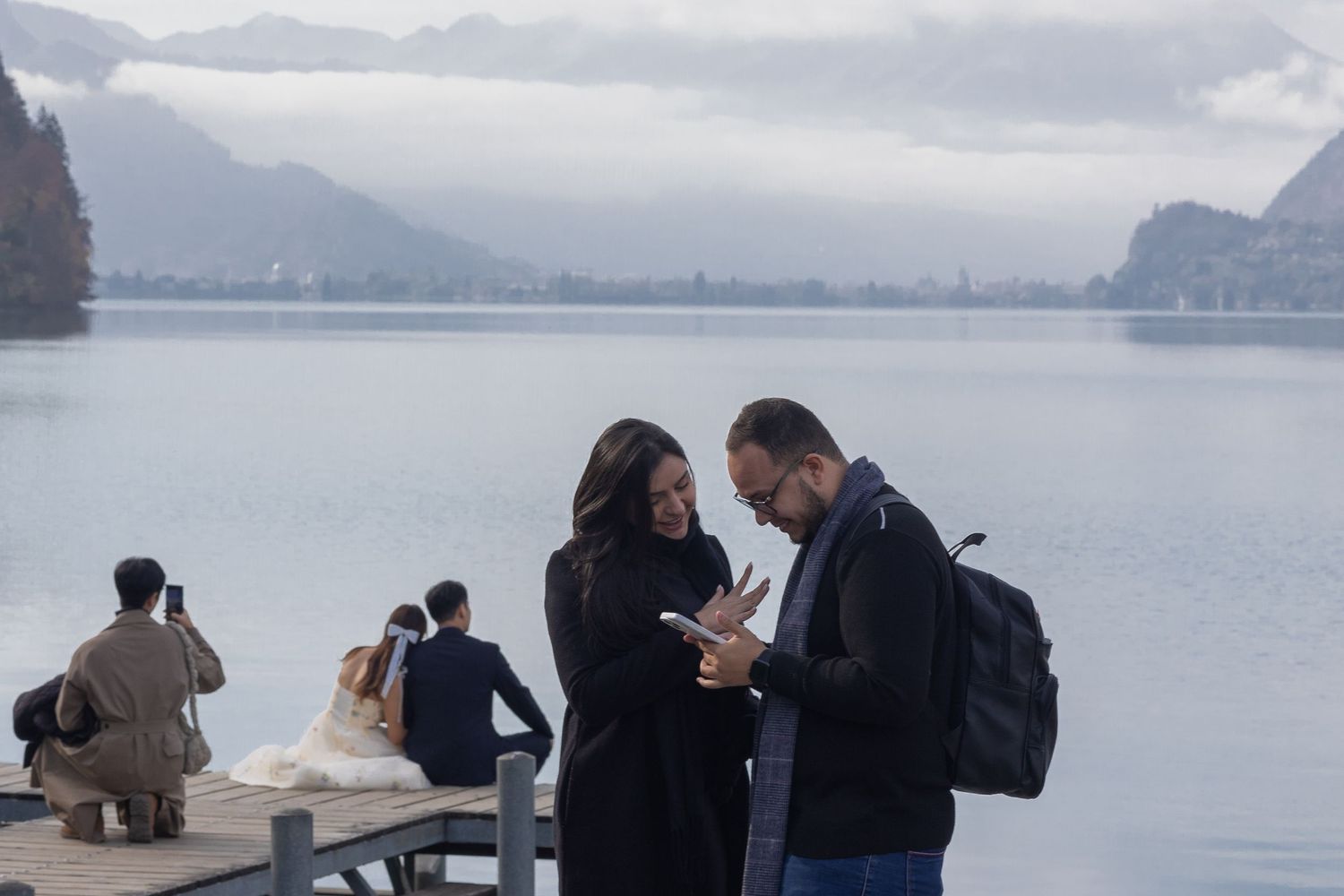 Couple sharing a moment on wooden pier with misty mountain lake backdrop.