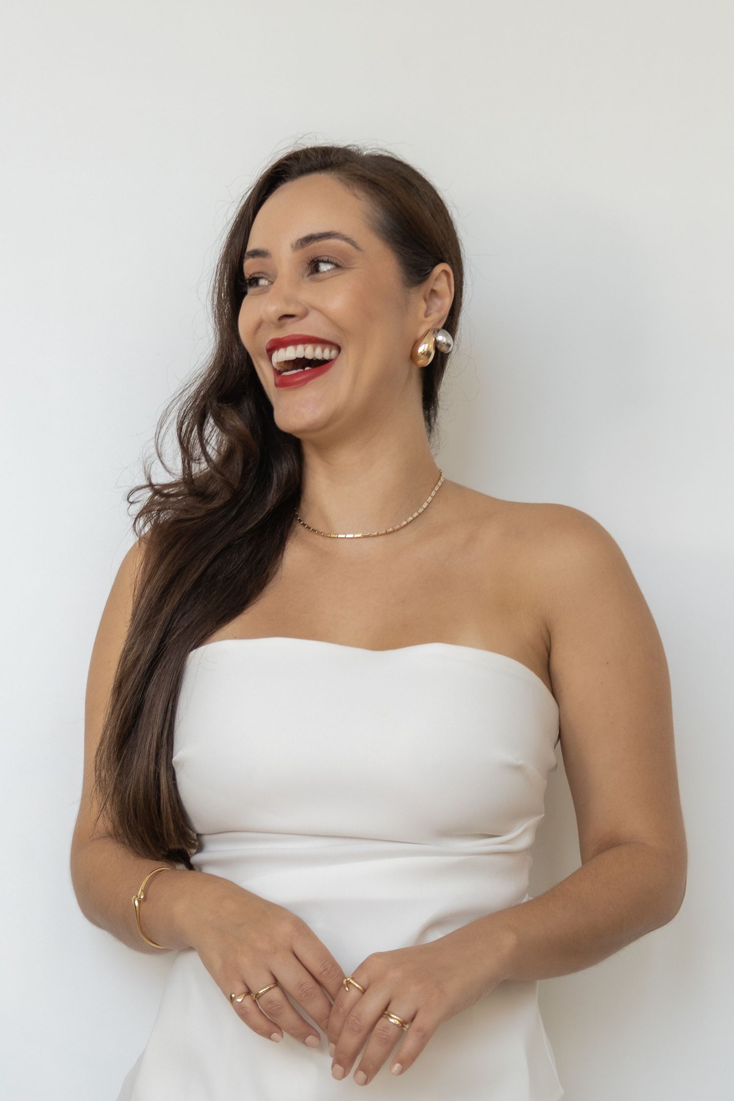 Joyful portrait of woman in white dress laughing against neutral background.