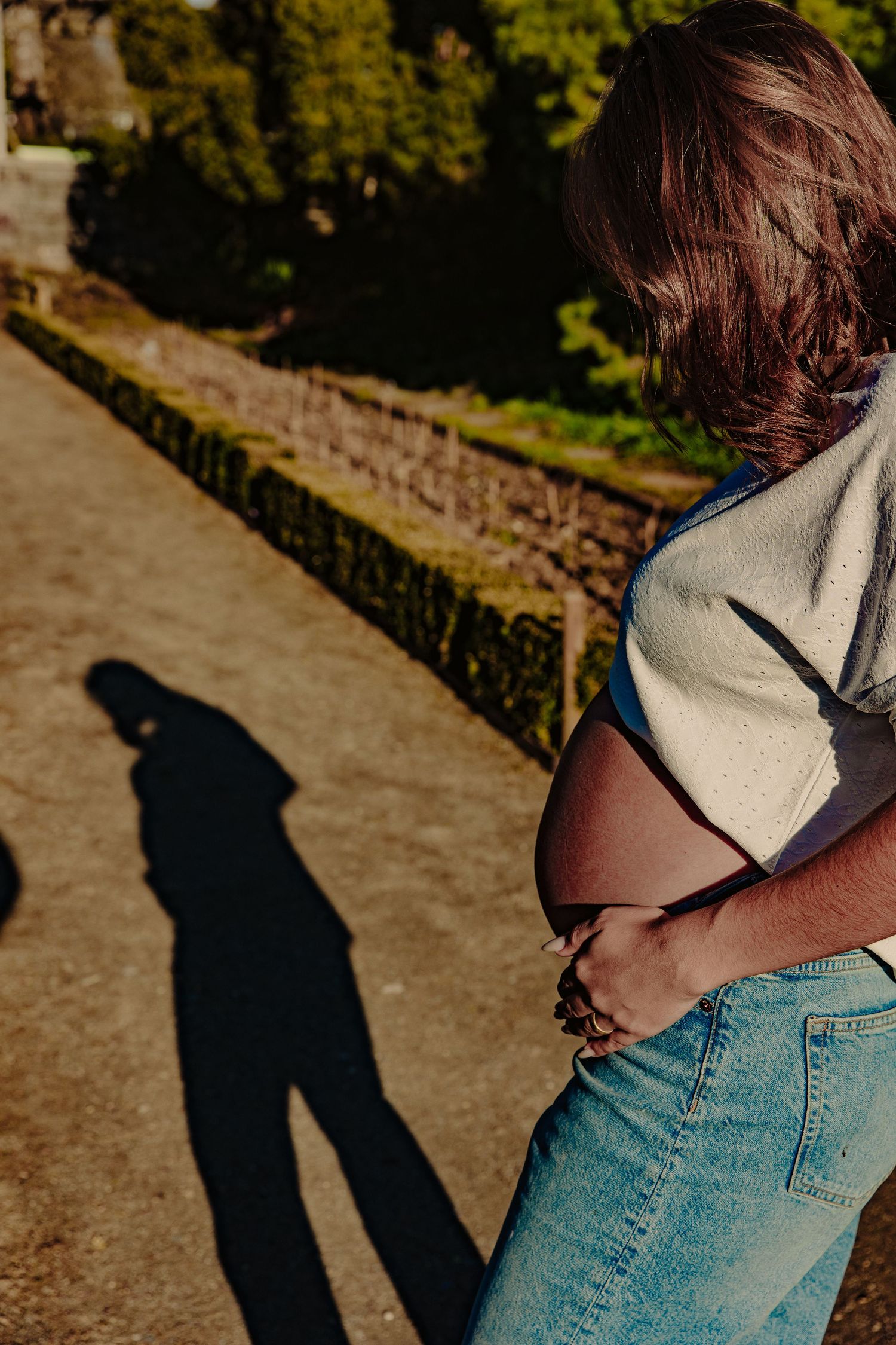 Side view of pregnant person's shadow cast on stone path during golden hour.
