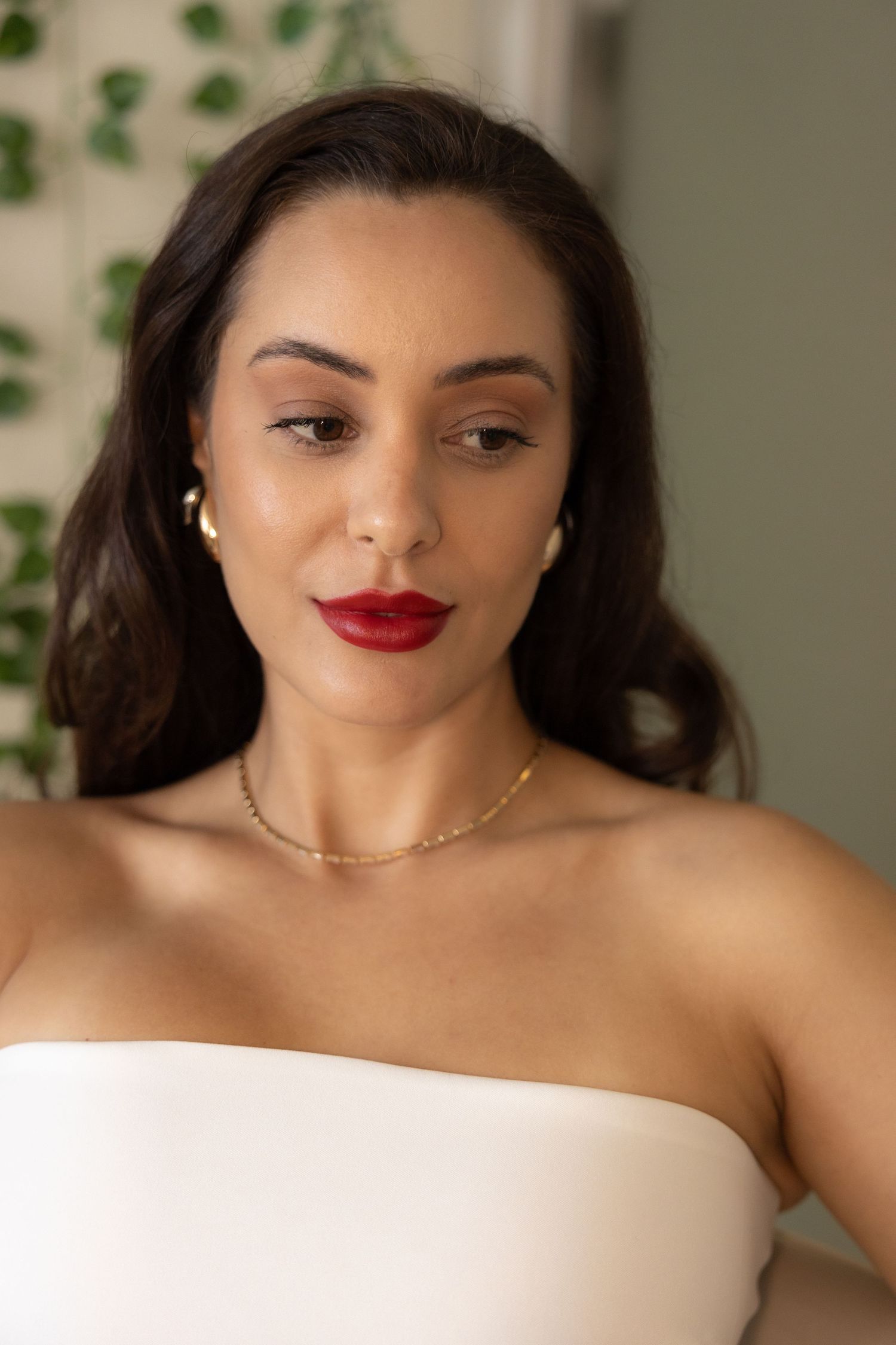 Elegant portrait of woman in white top with red lipstick and delicate gold necklace.