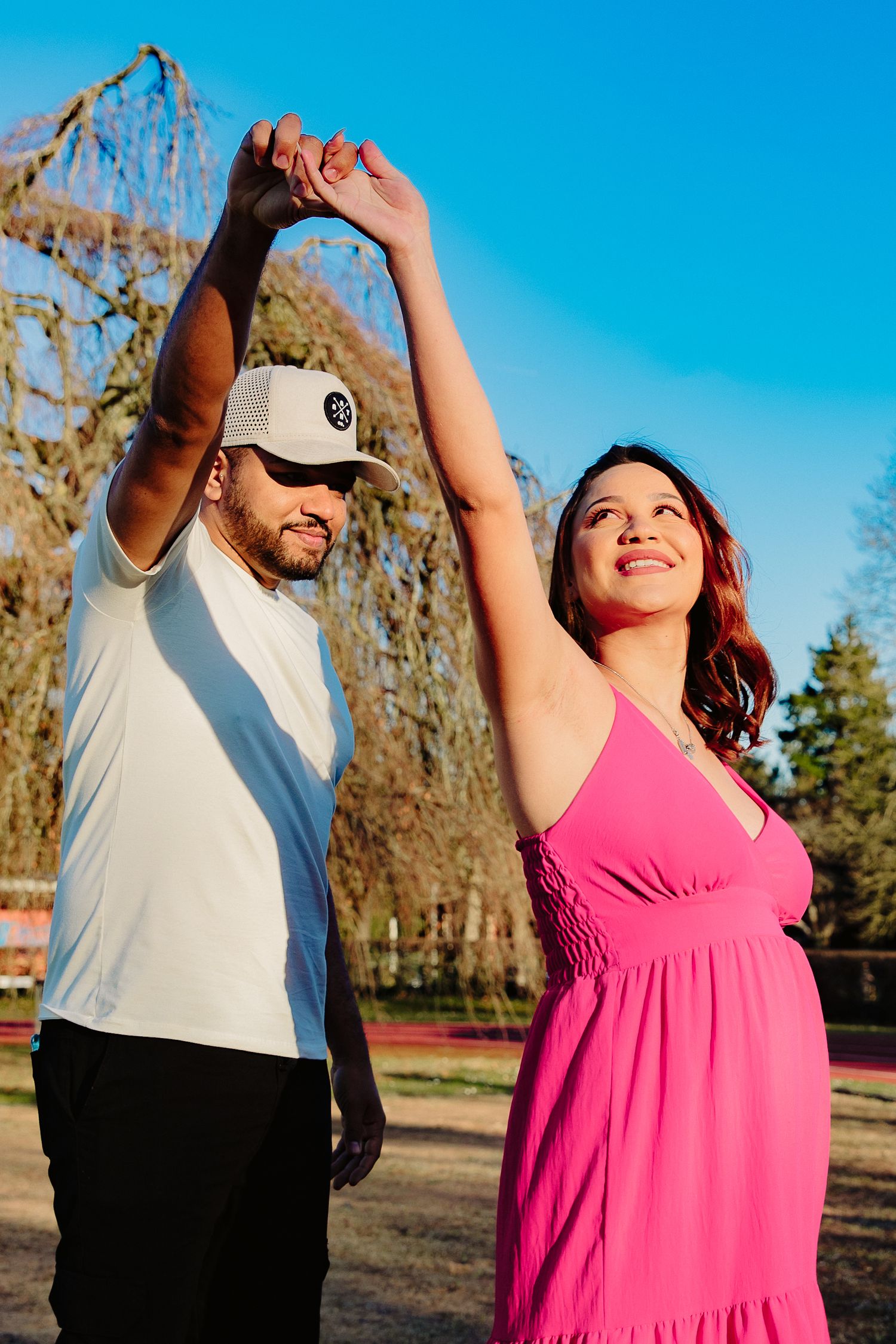 Couple dancing together outdoors in front of willow trees on a sunny day.