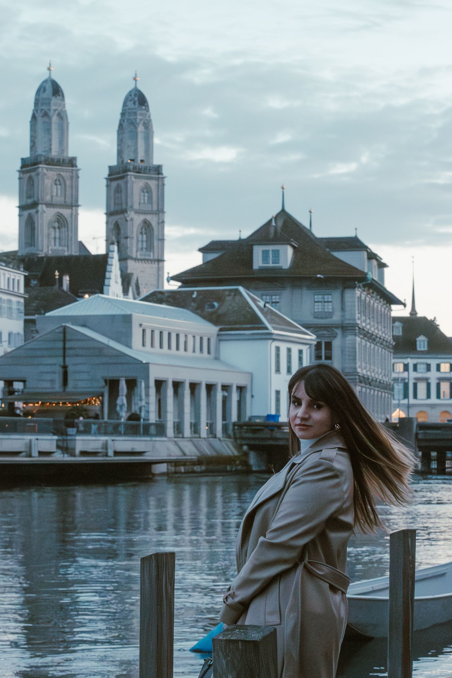 A scenic view of Zurich's Grossmünster cathedral with a person posing along the waterfront.