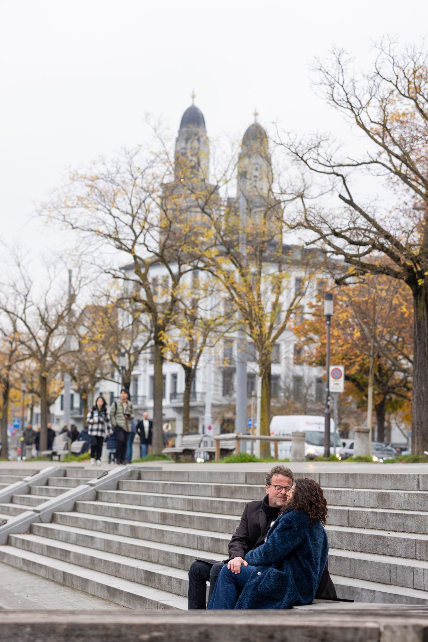 A couple sits on stone steps in front of a grand cathedral with twin spires during autumn.