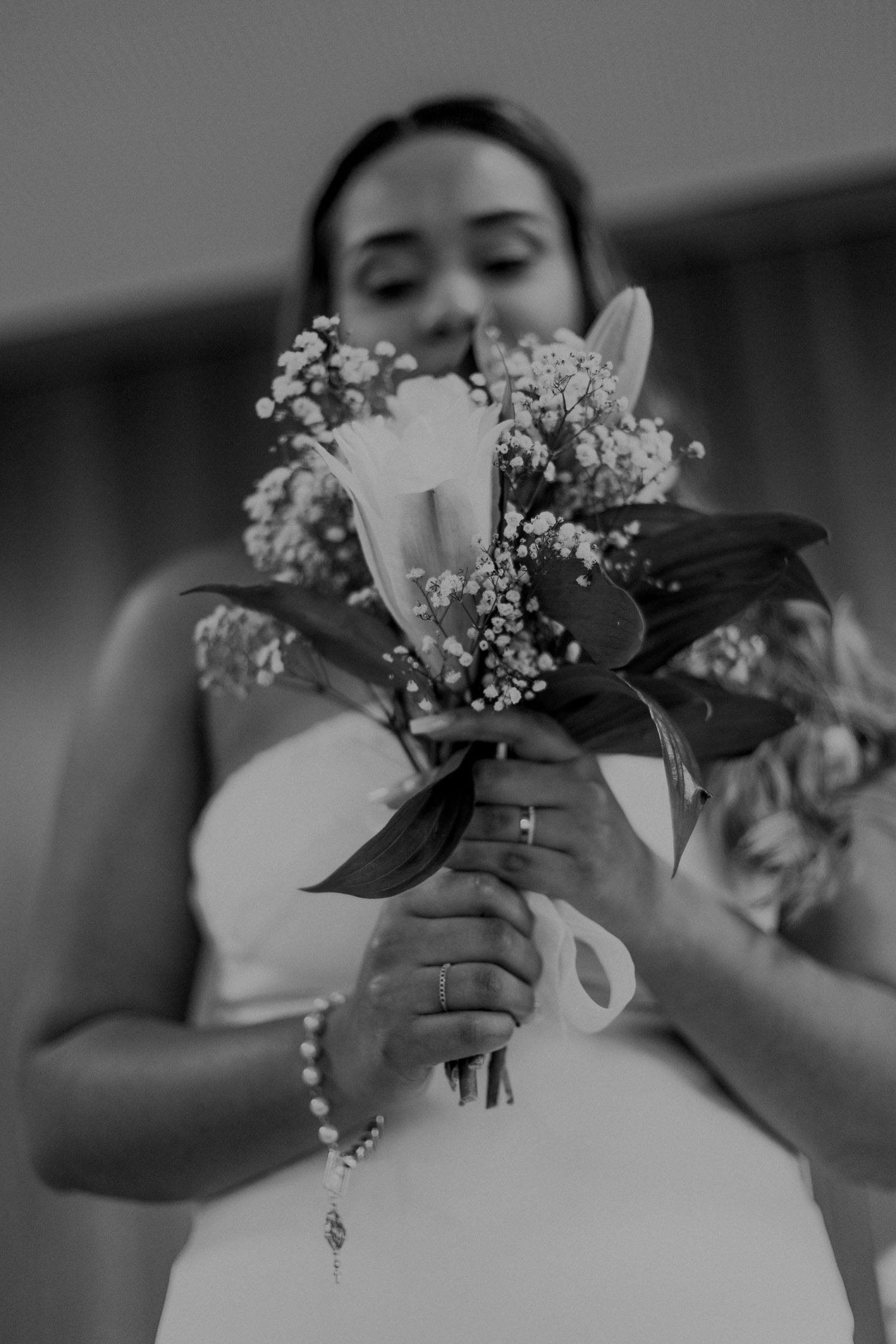 Black and white close-up of bride holding delicate bouquet with white flowers and baby's breath.