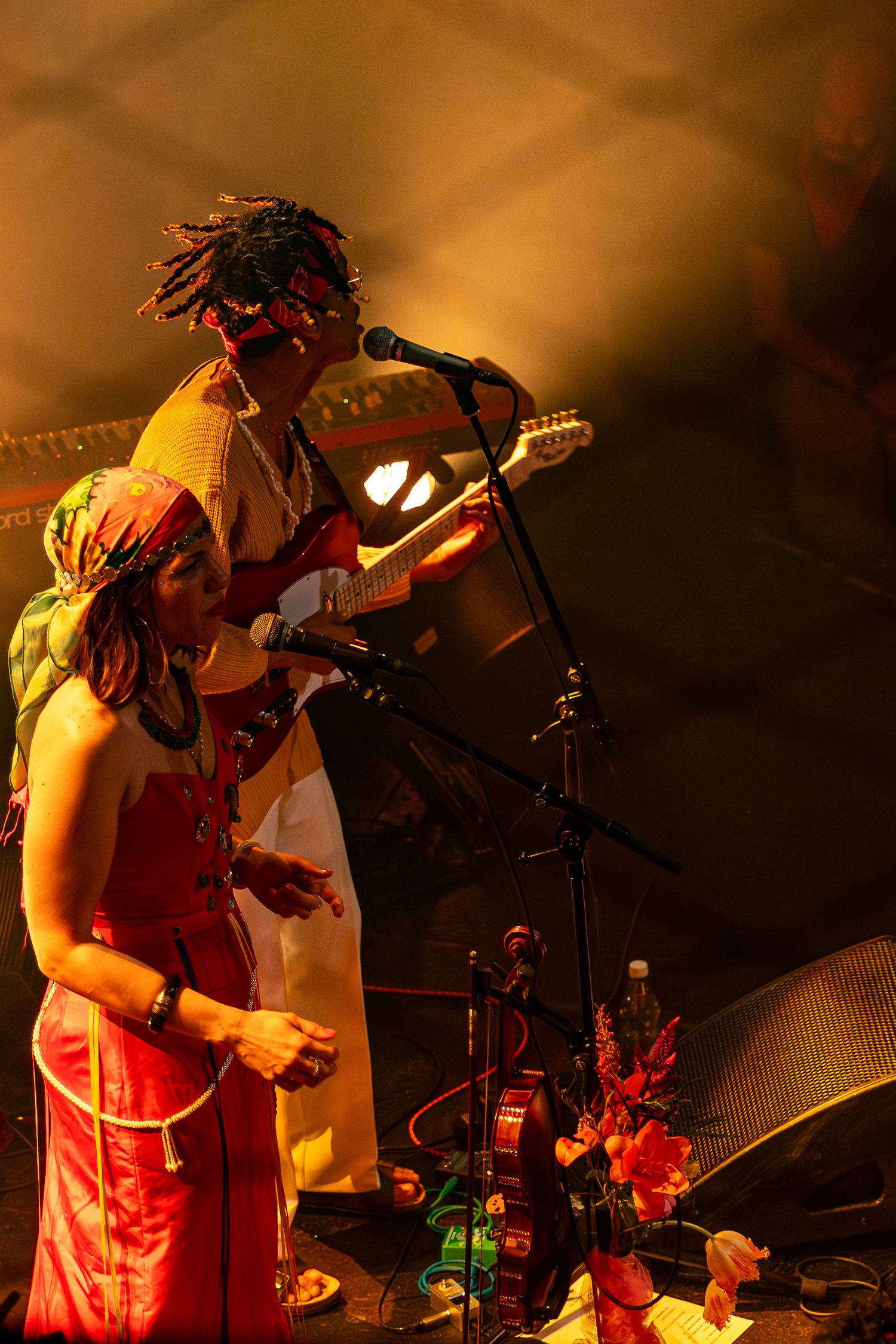 Musicians performing on stage with dramatic orange lighting and floral decorations.