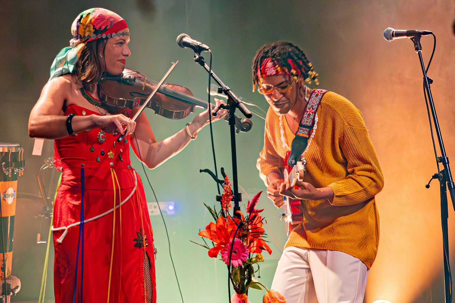 Musicians playing violin and guitar together on stage with red flowers.