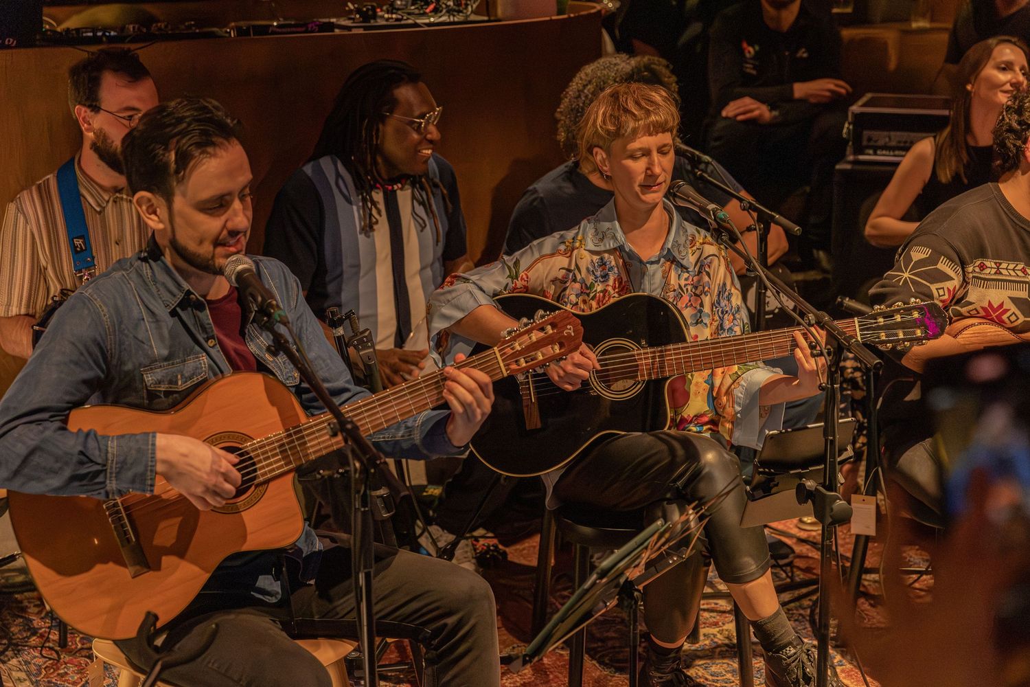 Musicians with acoustic guitars performing together on stage in warm lighting.