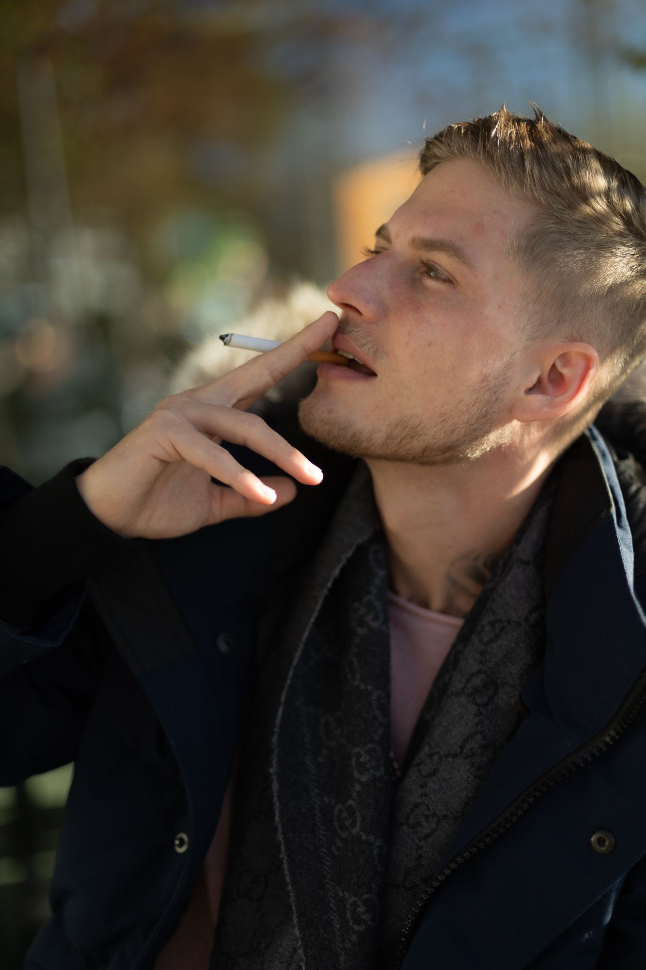 Person in dark coat smoking a cigarette in moody outdoor lighting.