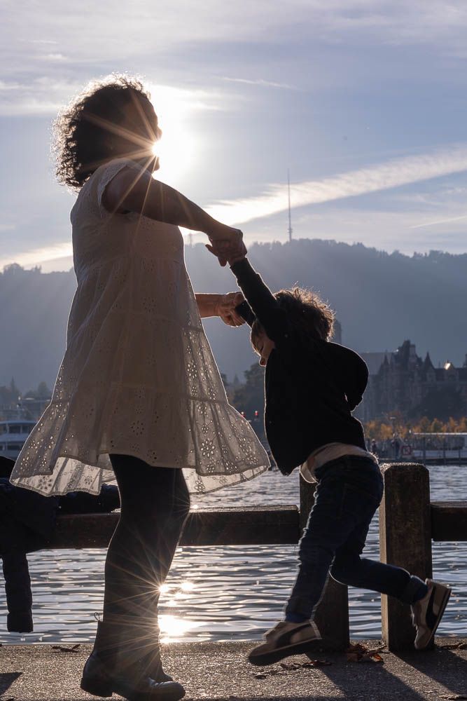Silhouetted figures playing and dancing together by the water during sunset, creating a magical backlit moment.