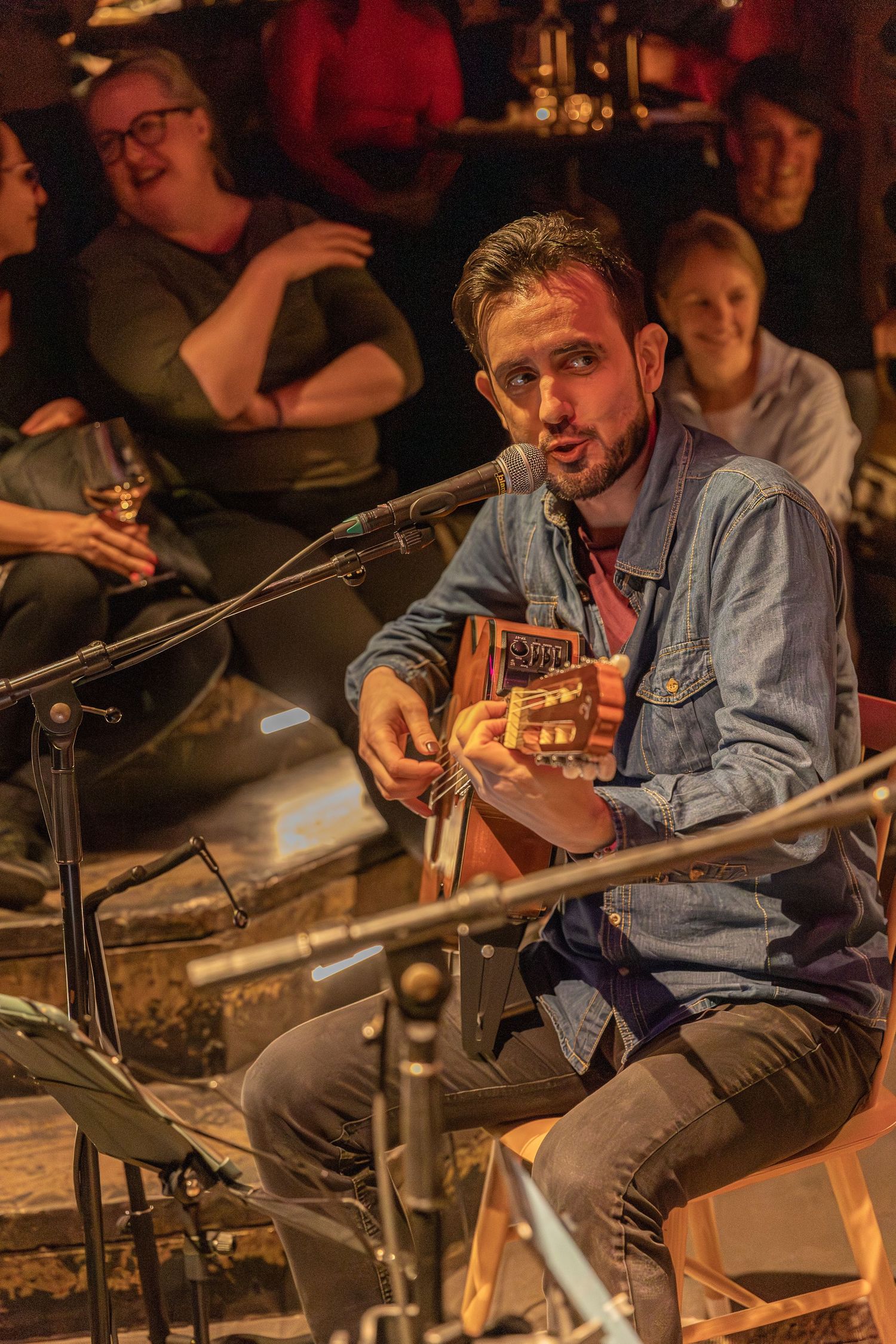 Musician playing acoustic guitar and singing into microphone during intimate performance.