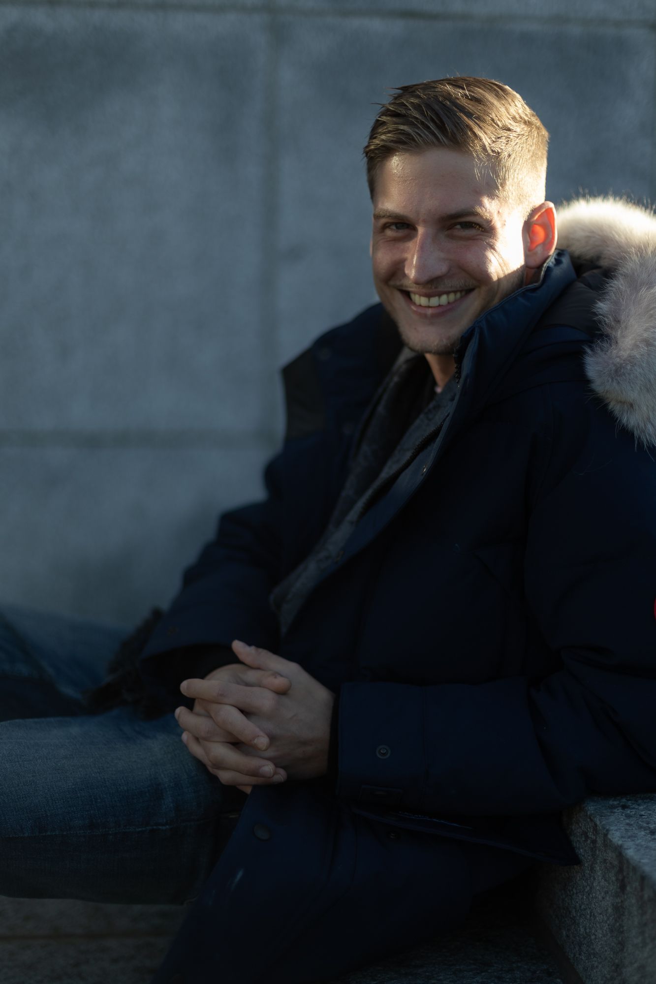 Portrait of person in dark fur-trimmed coat smiling in shadowy lighting.