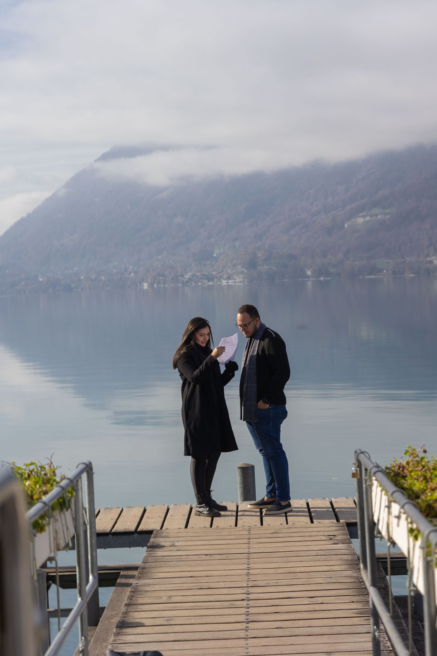 Couple standing on wooden dock with scenic mountain lake view in background.