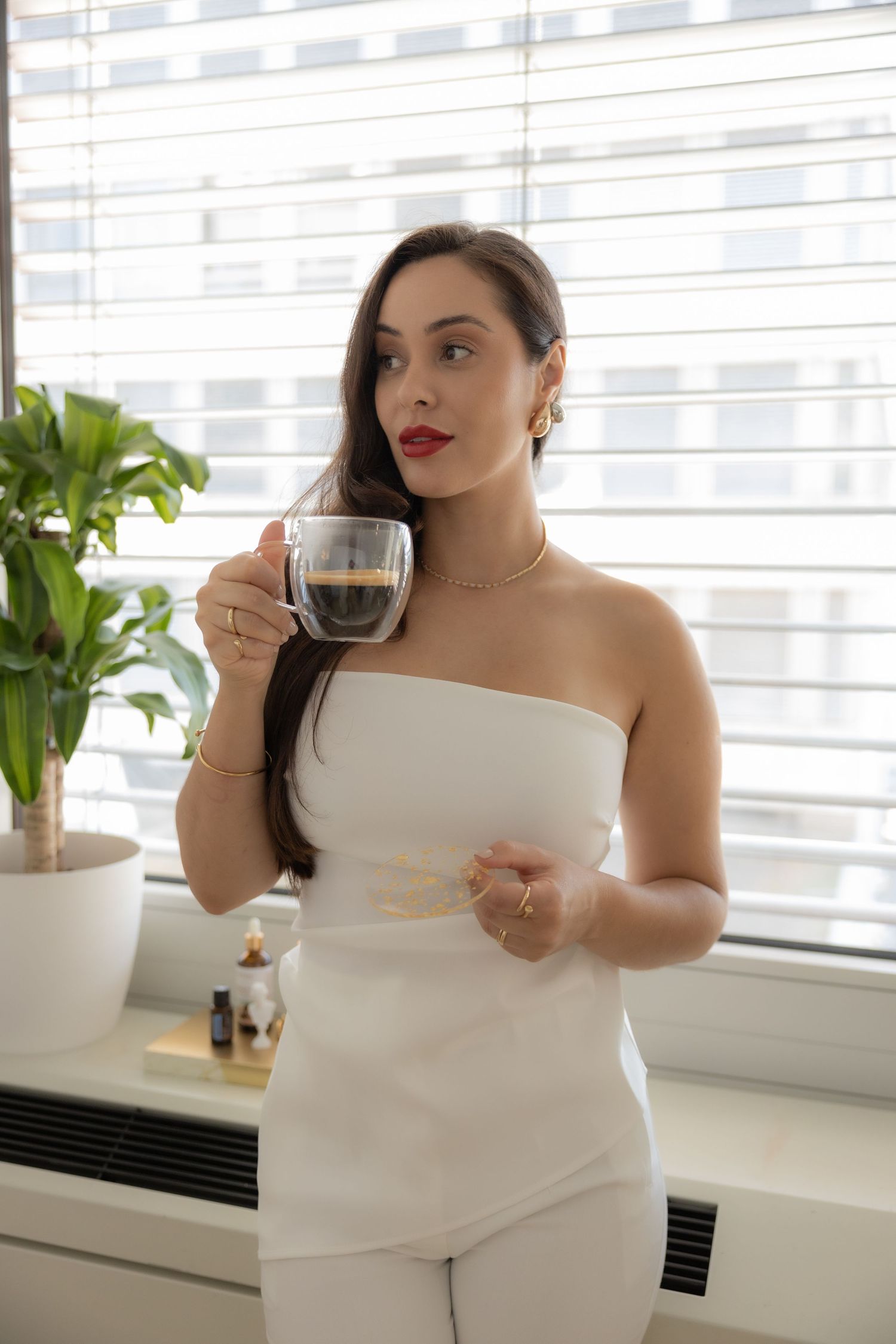 Woman in white ensemble sipping coffee by sunlit window. female portrait photographer in Zürich