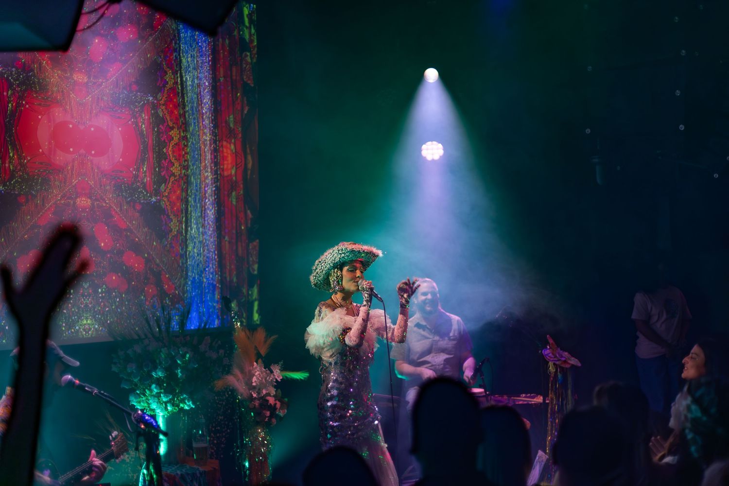 A performer in a spectacular costume sings on stage under dramatic colorful lighting.
