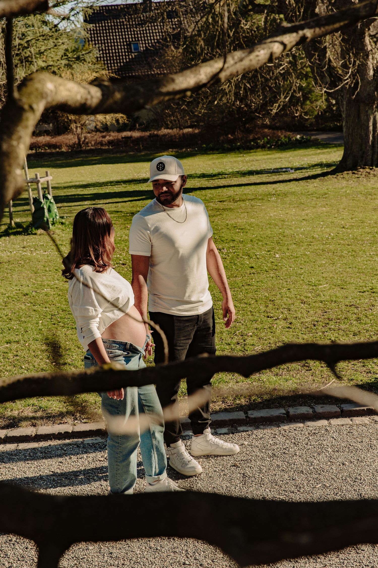 Happy couple in matching white tops standing together on gravel path in park.