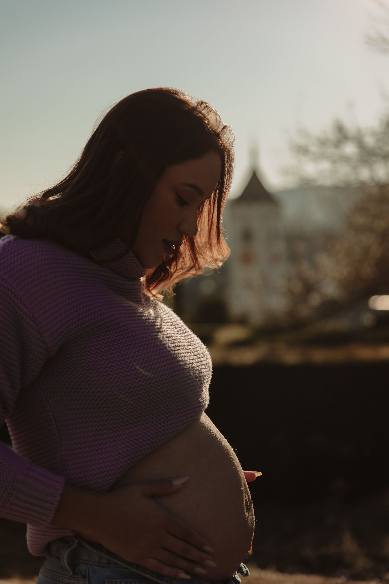 Maternity portrait in purple sweater against sunset with castle backdrop.
