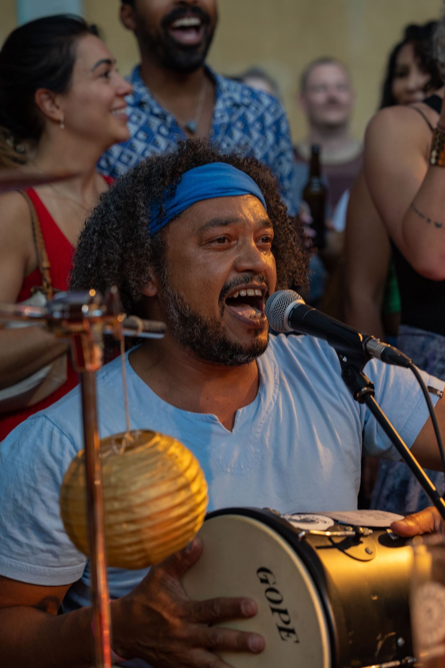 Musician singing passionately while playing percussion at vibrant indoor celebration.