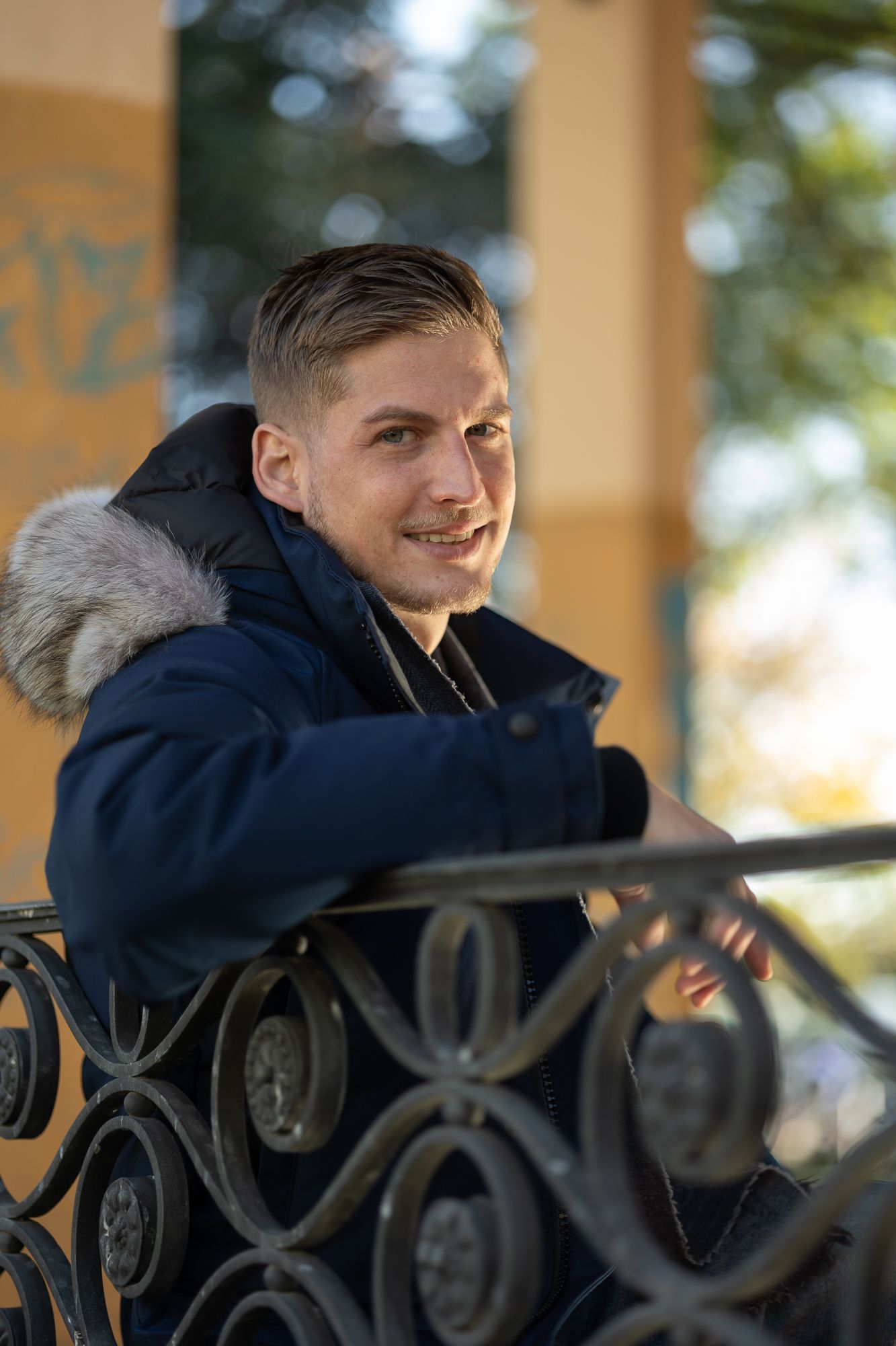 Outdoor photo by ornate metal railing wearing a fur-trimmed navy parka.