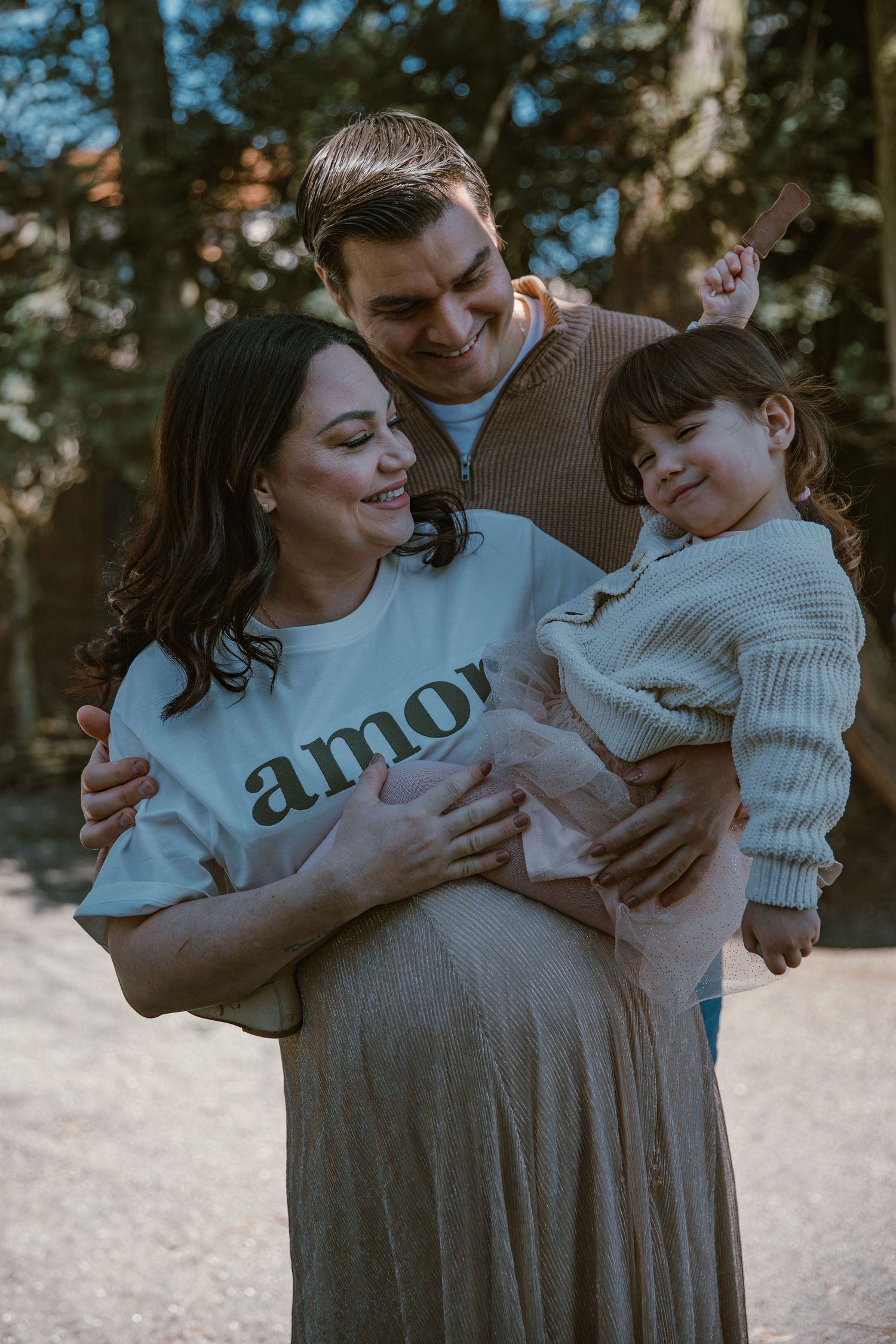 A family sharing a tender moment outdoors wearing cozy sweaters with the parent wearing an 'amor' shirt.