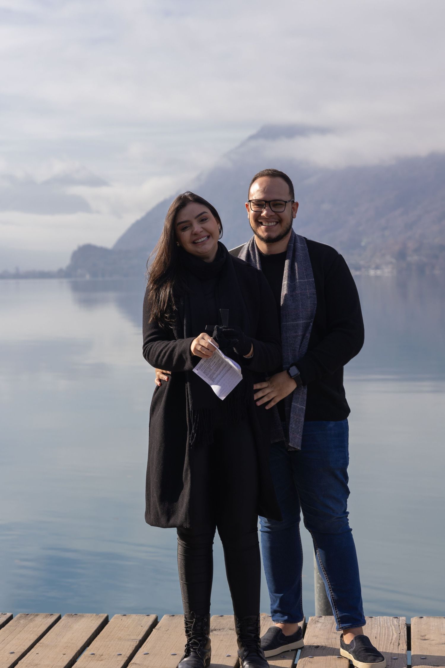 Happy couple poses together on wooden dock overlooking serene mountain lake.