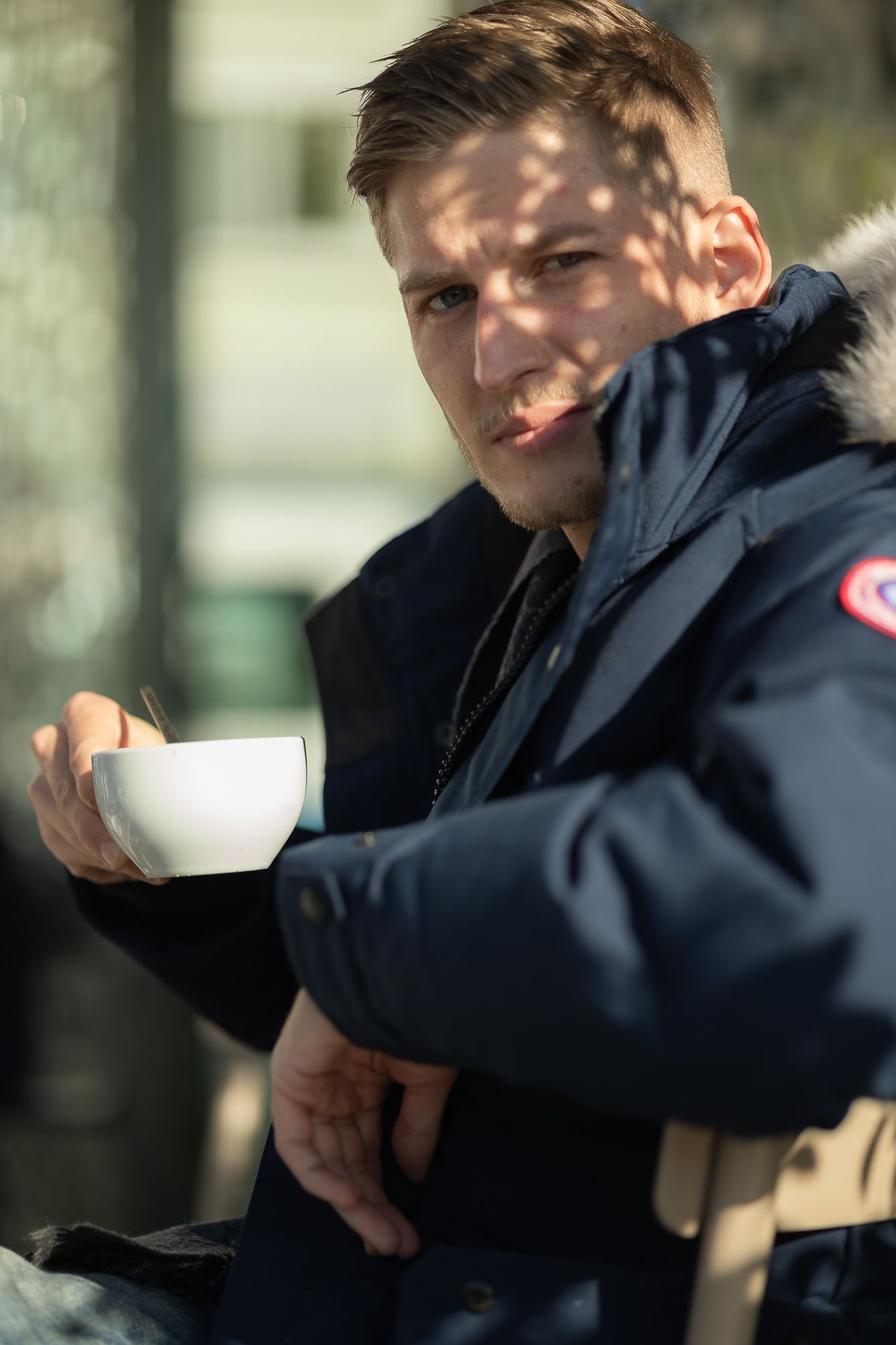 Casual outdoor coffee moment wearing a branded navy parka with fur trim.