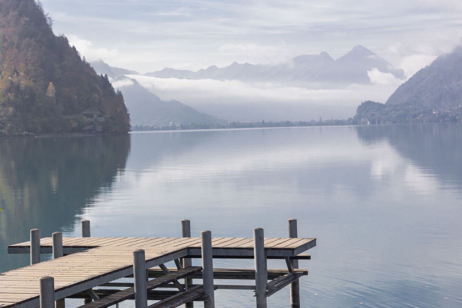 Serene mountain lake landscape with wooden dock and misty peaks in background.